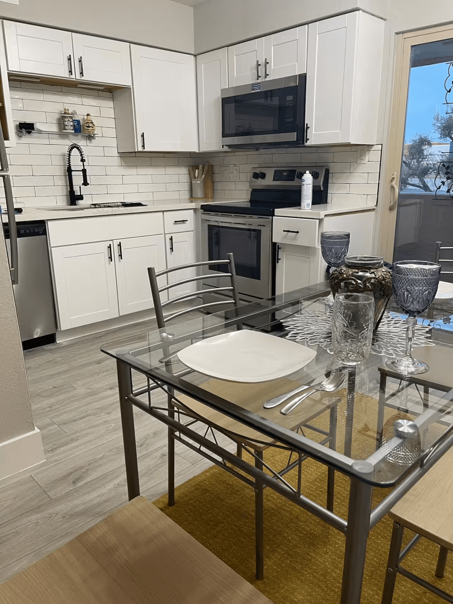 Modern kitchen with white cabinets, stainless appliances, and a glass dining table set for two