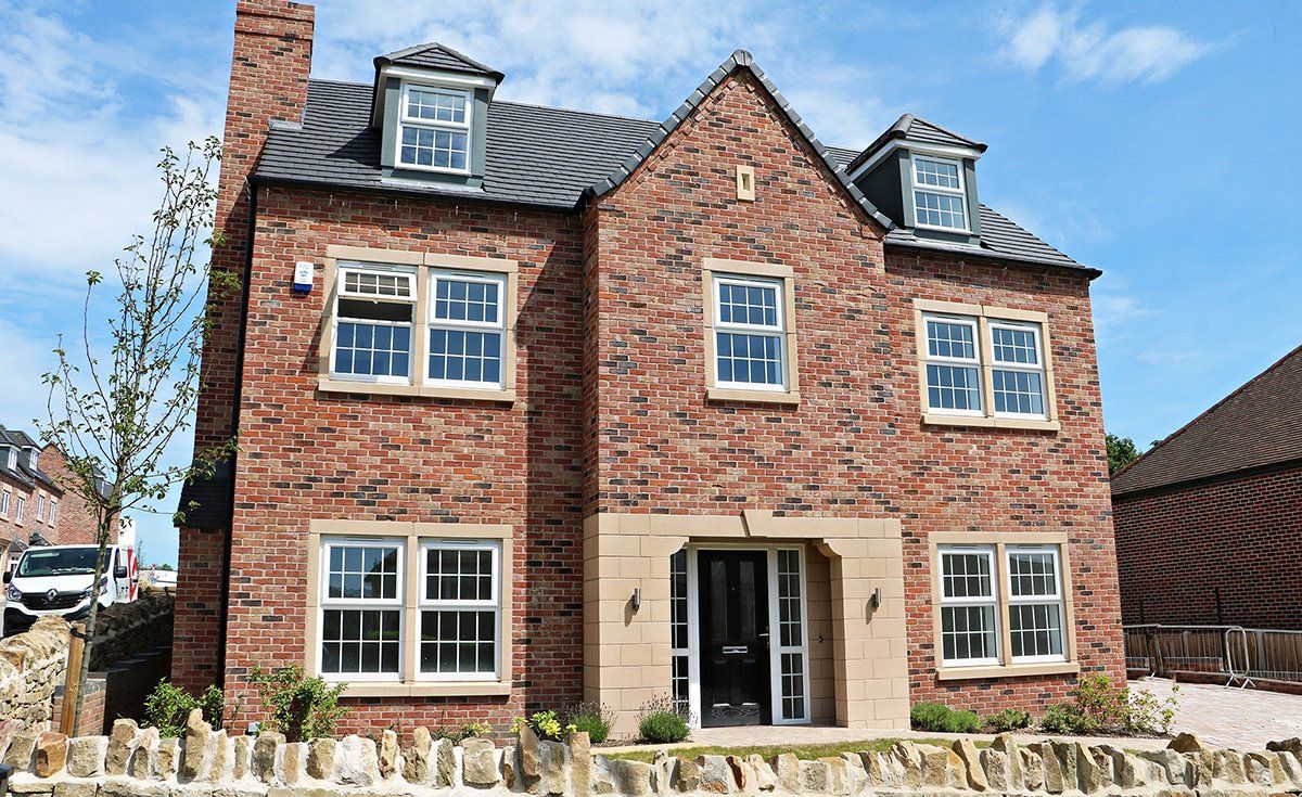 Two-story red brick house with a dark roof and sandstone accents; blue sky background.