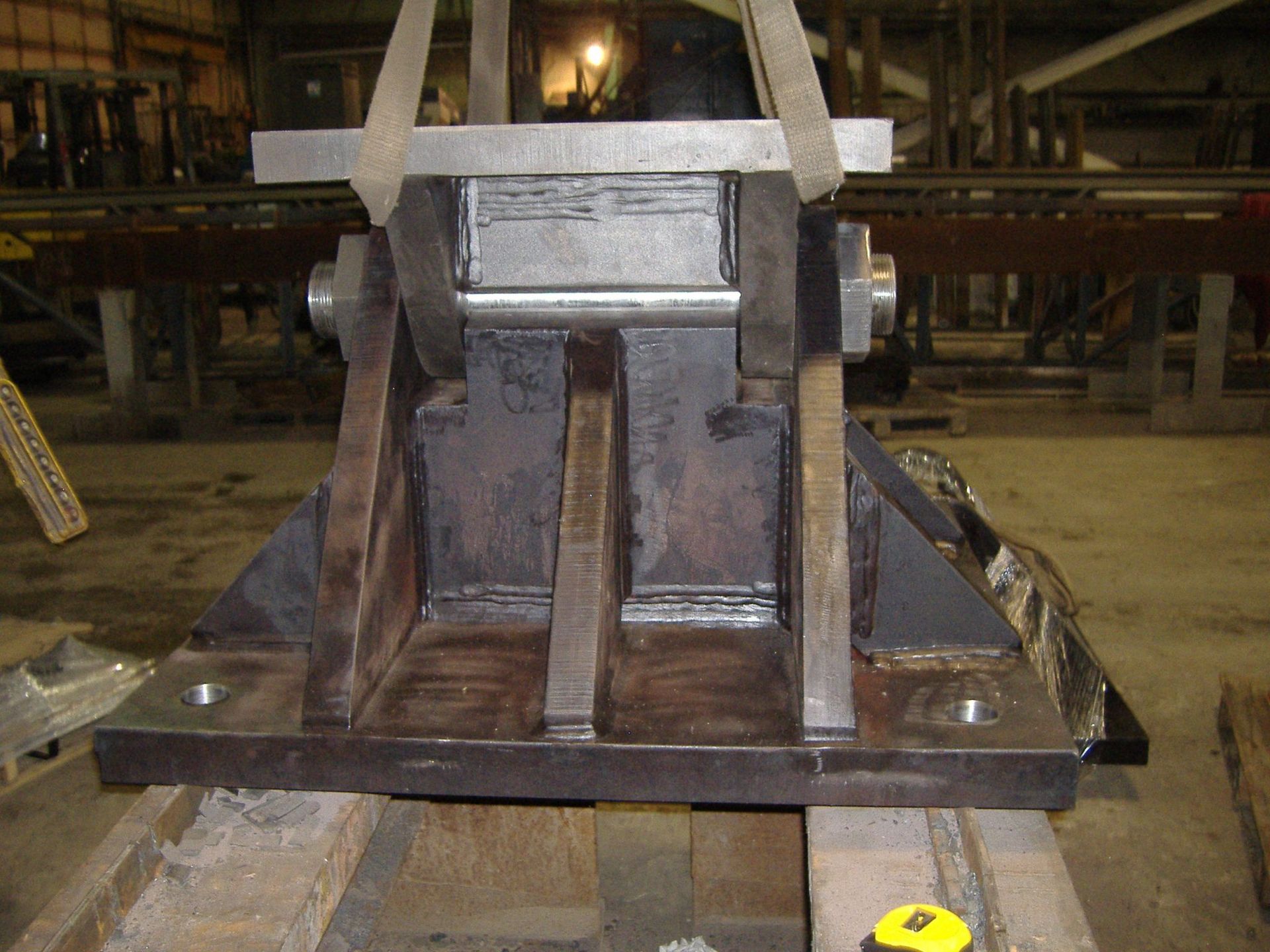 Steel bracket, dark metal, being lifted by straps, likely in a workshop.