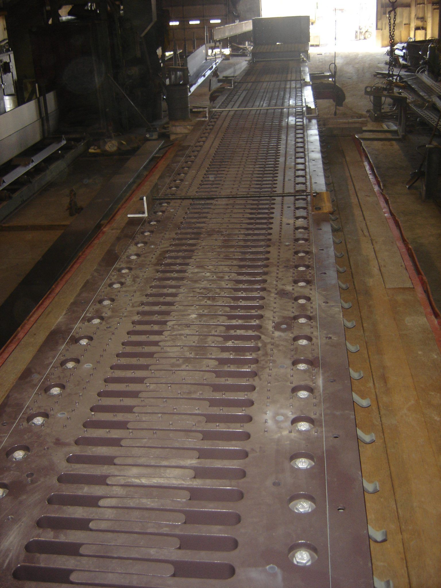 Large industrial metal surface with slotted segments and numerous circular holes.