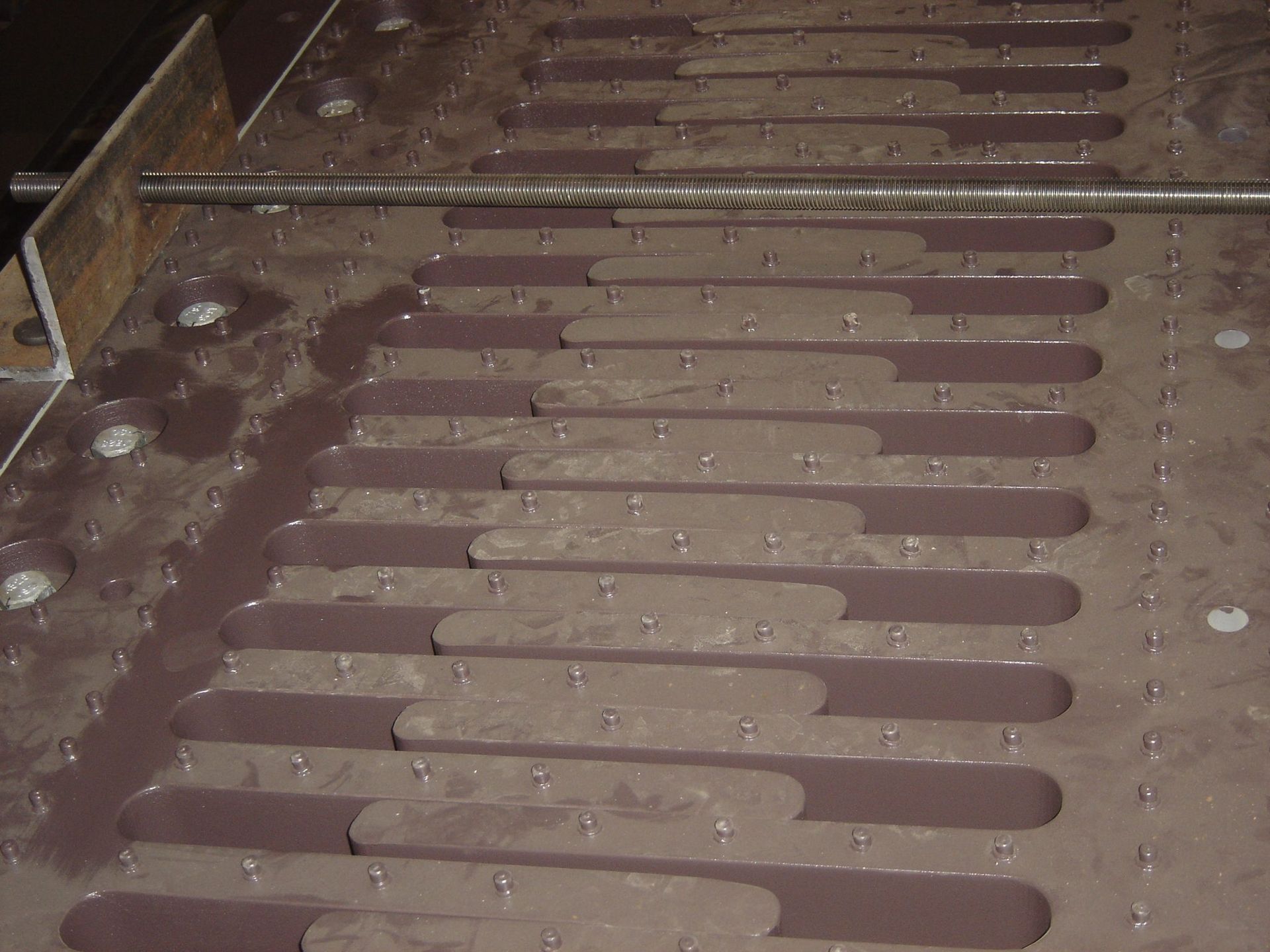 Metal surface with rectangular slots filled with a thick, brown substance, with a metal bar across it.