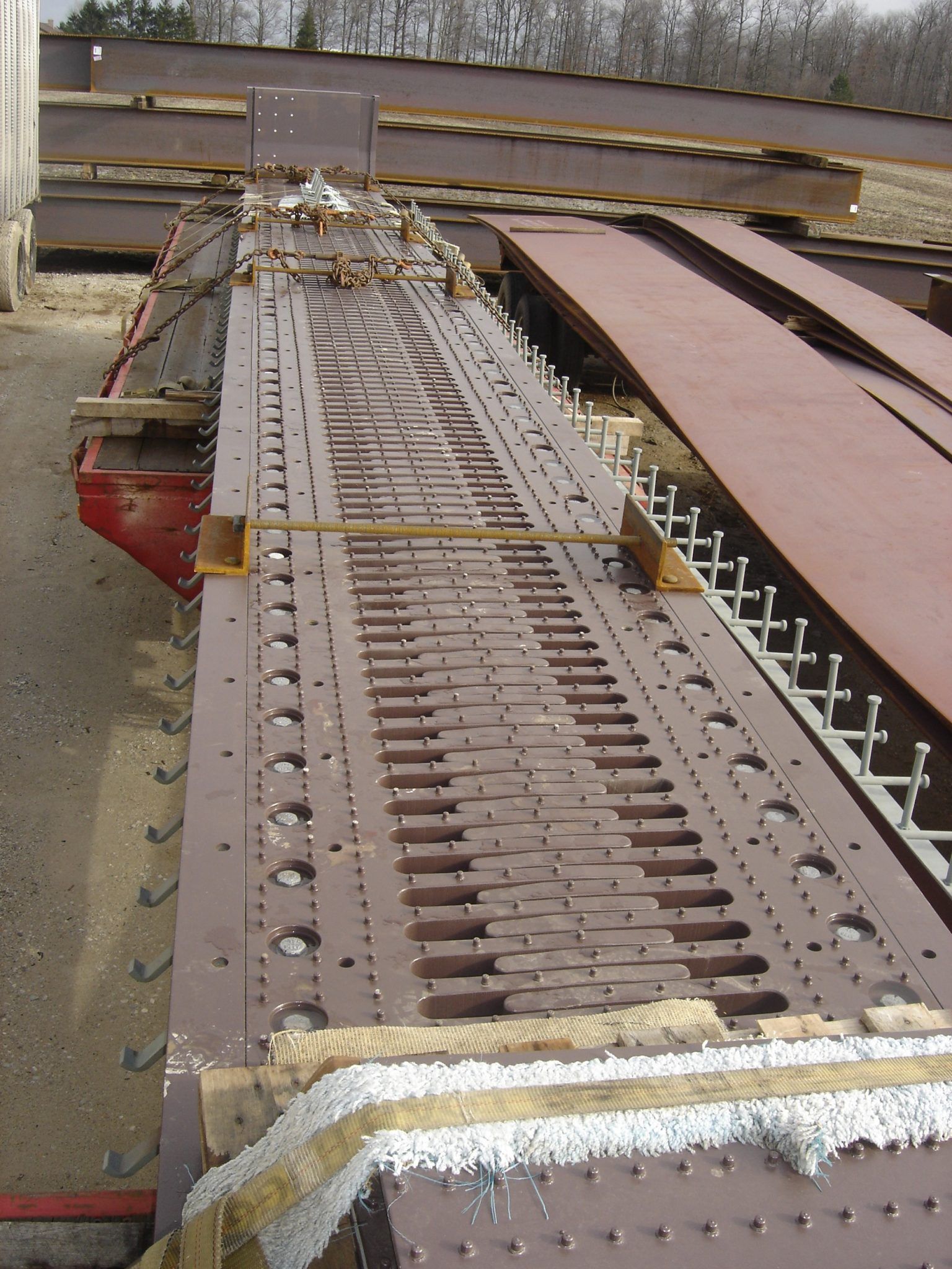 Metal bridge component with rivet holes, support beams, and brown steel plates on construction site.