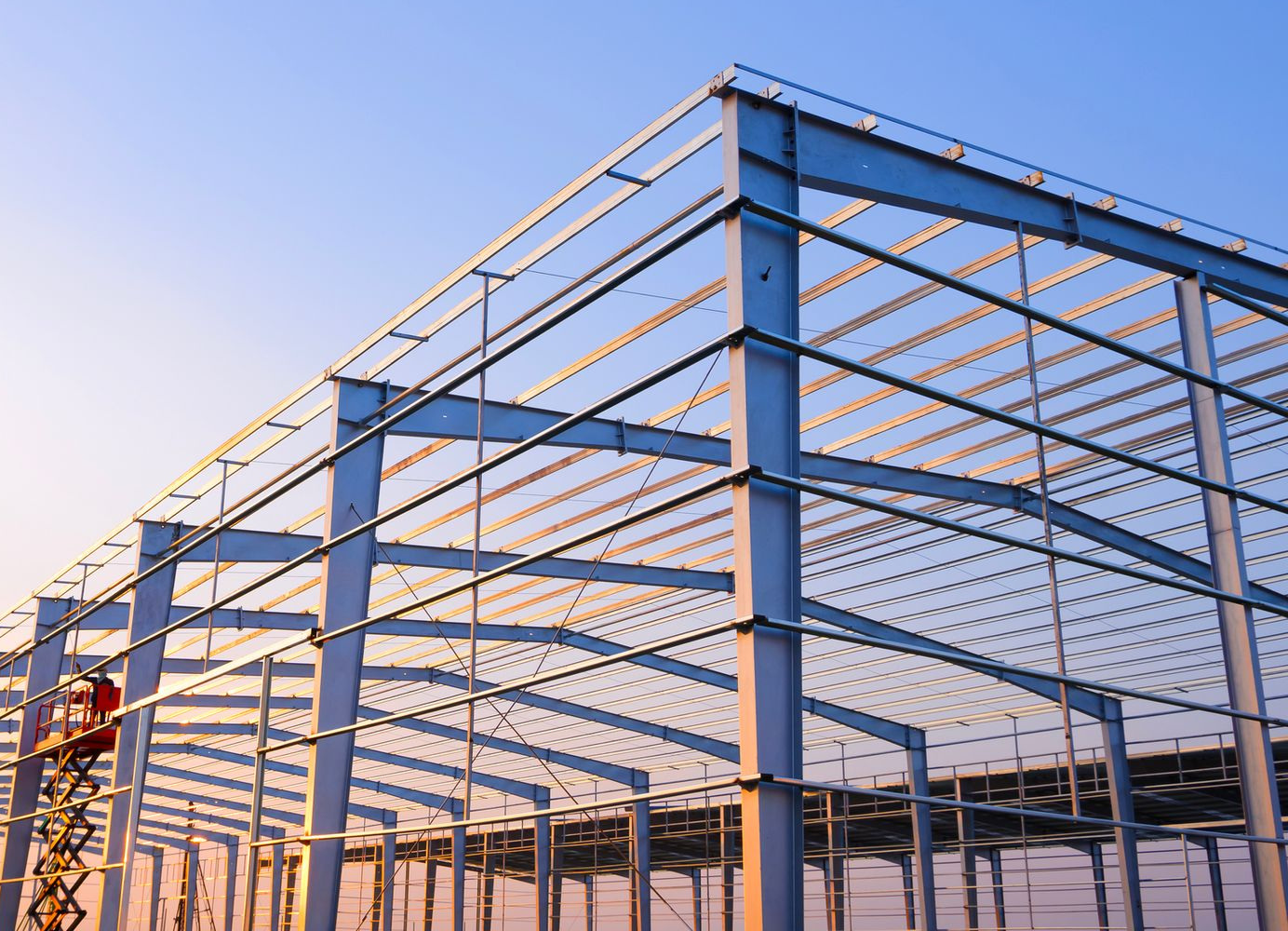 Steel-framed industrial building under construction against a clear blue sky.