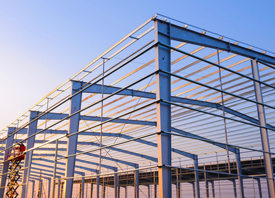 Steel-framed industrial building under construction against a clear blue sky.