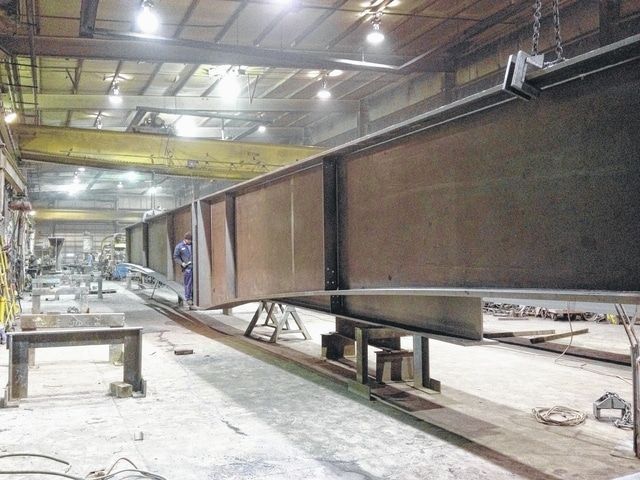 Large steel beam in a workshop, supported by stands, under a crane.