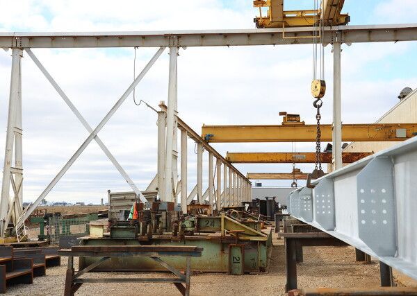 Steel beam being lifted by a yellow industrial crane in a metalworking shop.