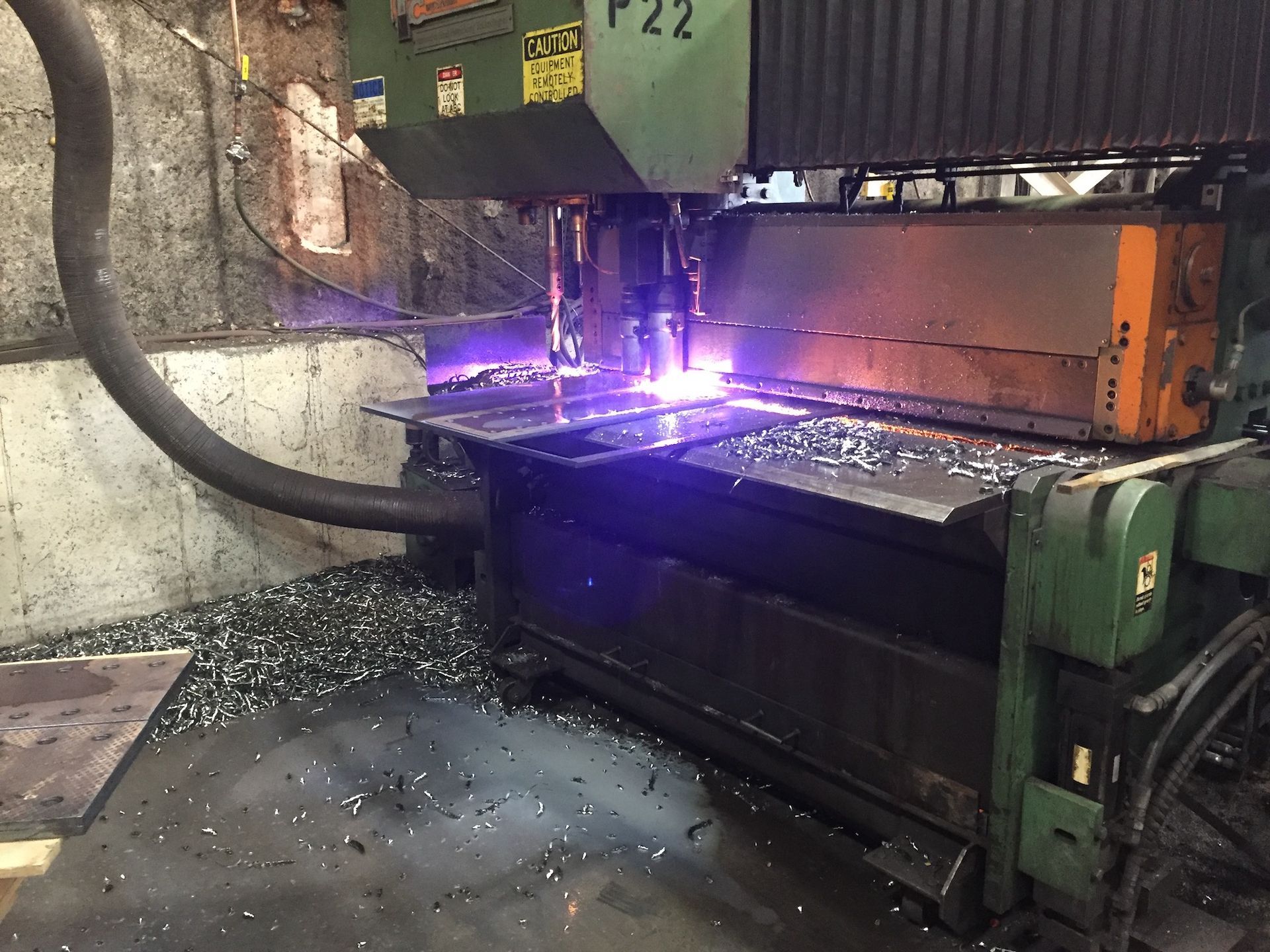 Plasma cutter machine cutting metal; sparks and bright purple light in industrial setting.
