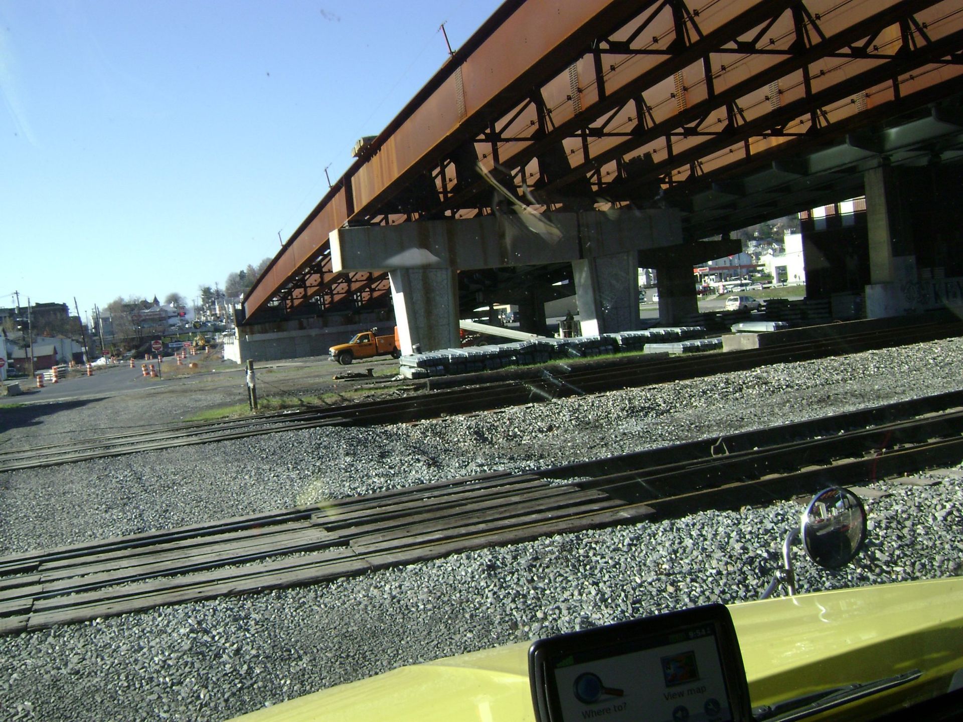 Railroad tracks beneath an elevated structure under construction on a sunny day.