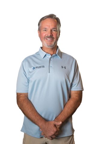 Smiling man in a light blue polo shirt standing against a white background with hands clasped.