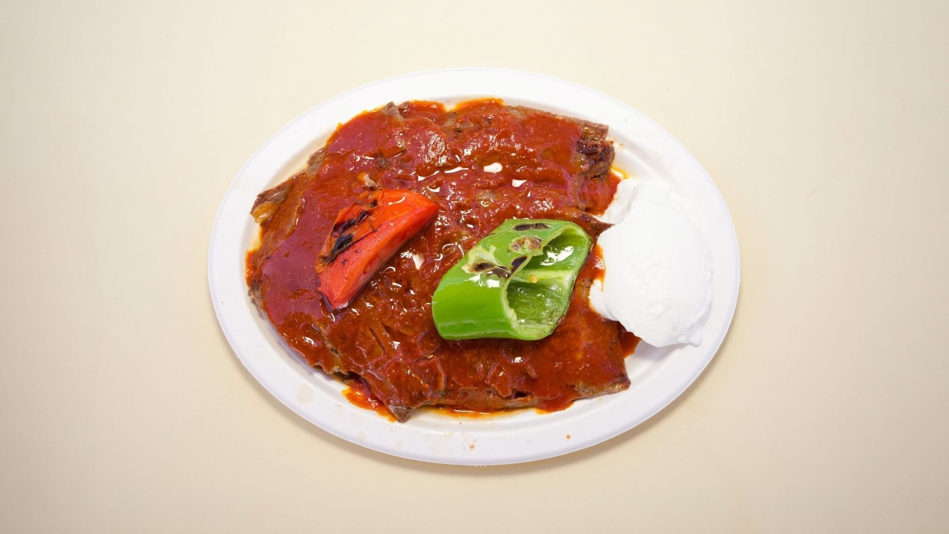 White plate with red saucy dish topped with green basil and a slice of red pepper