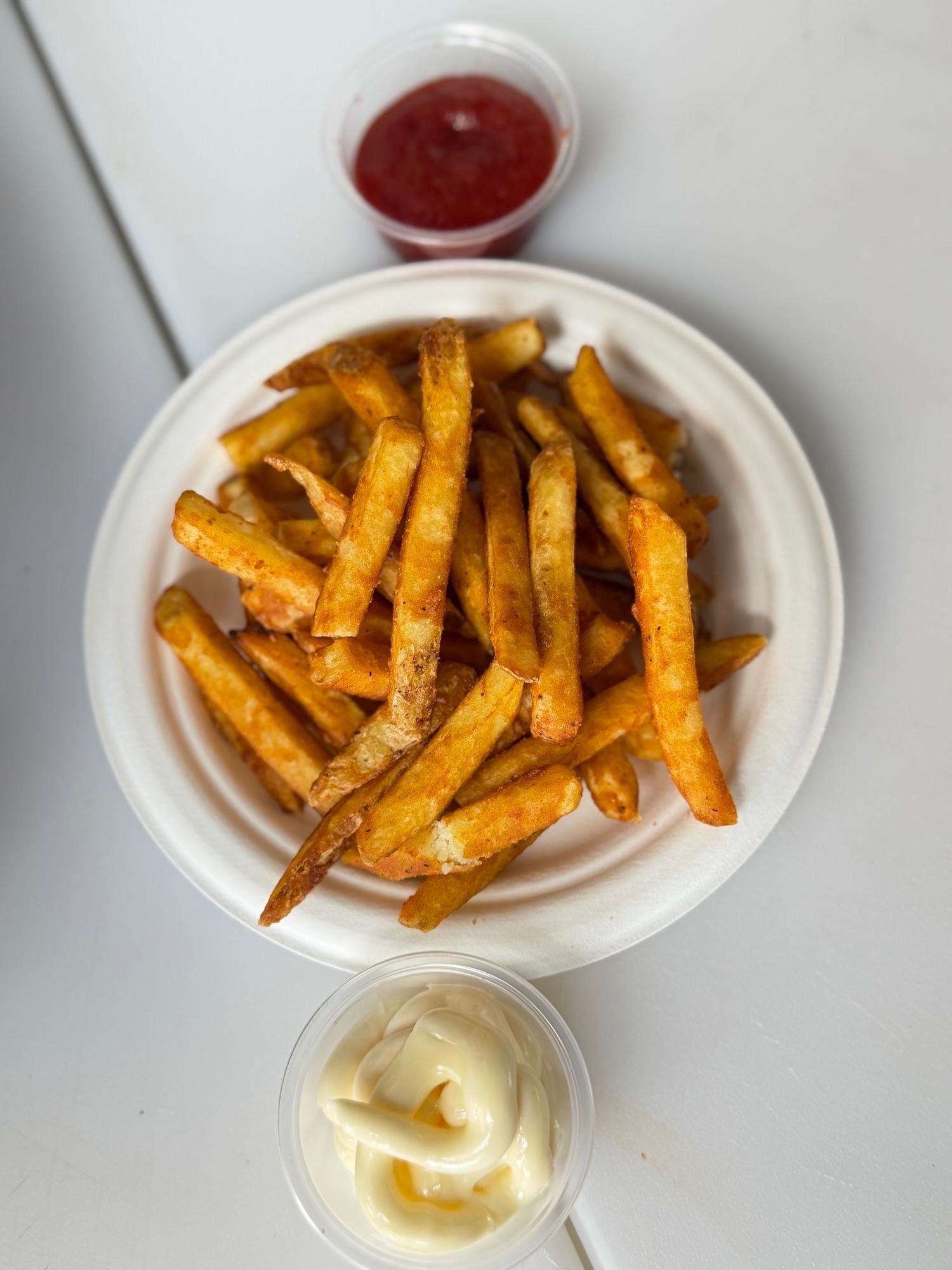 Bowl of seasoned fries with red dipping sauce and a small cup of mayonnaise on a light table