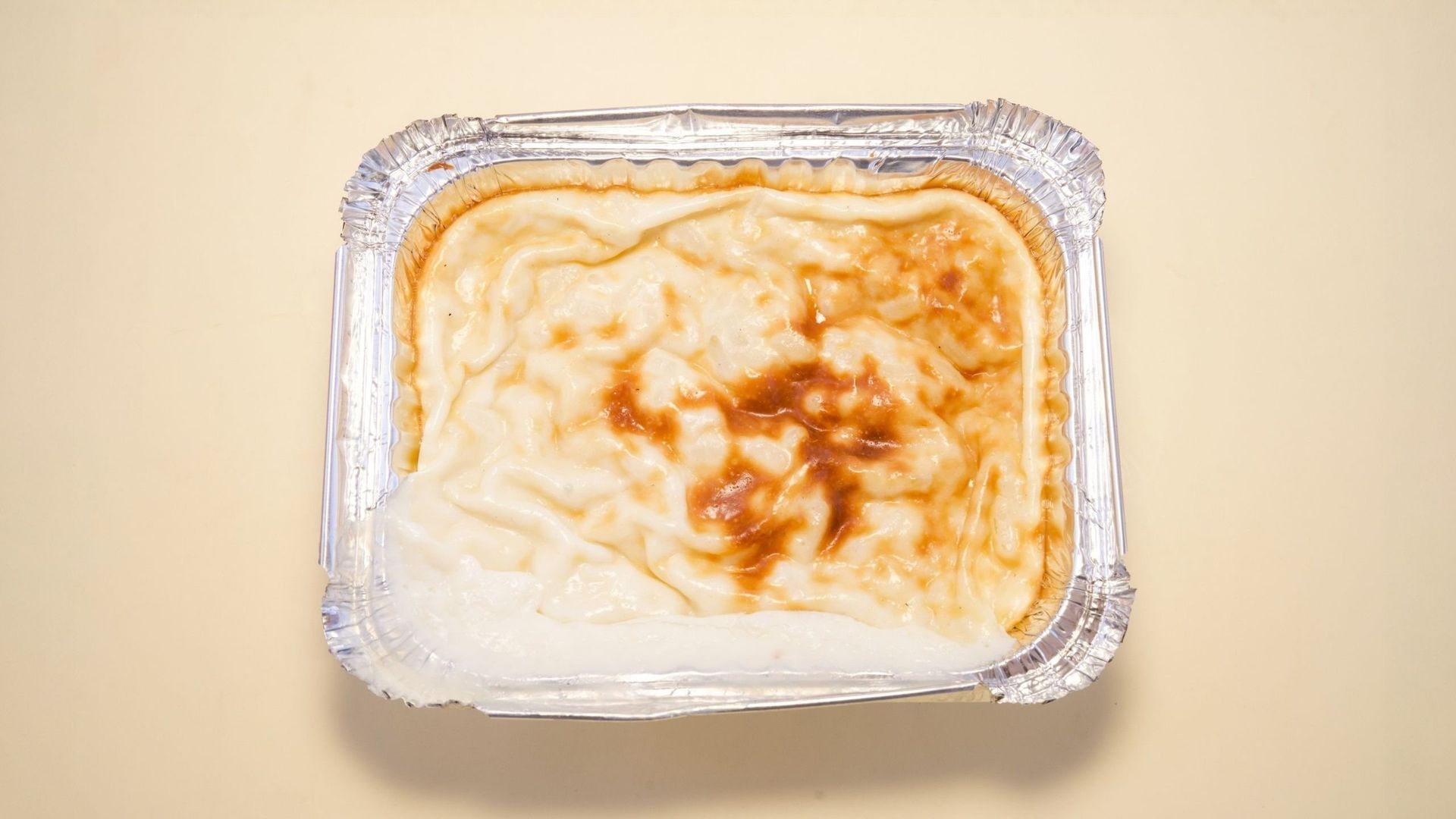 Foil tray of creamy baked dessert with a golden-brown top on a beige background