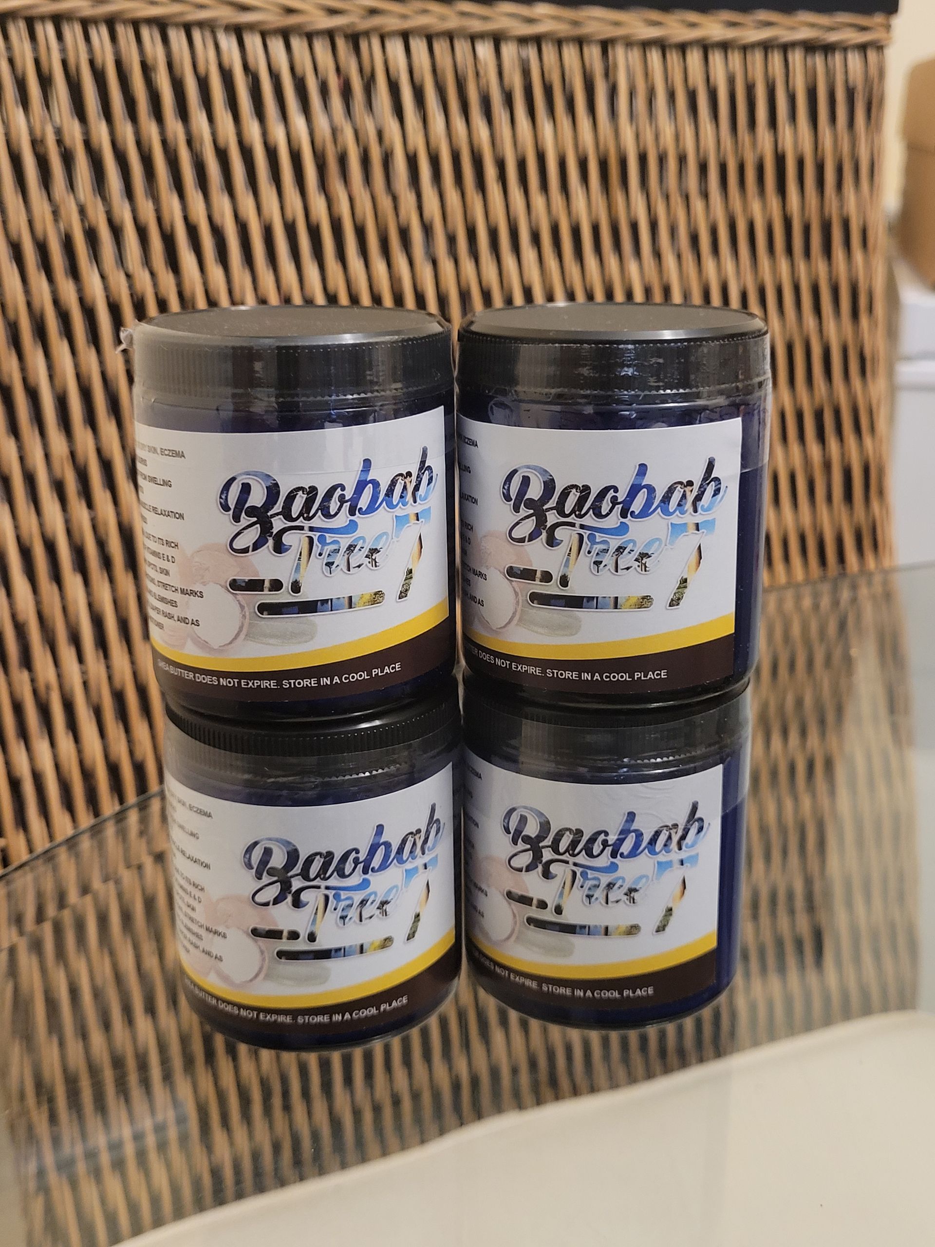 Four stacked black-lidded jars with white labels on a woven wicker background