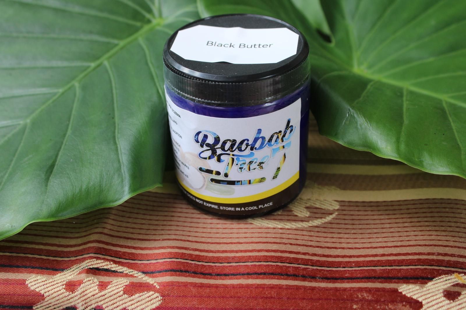 Small herbal supplement jar on a patterned cloth, framed by large green leaves.