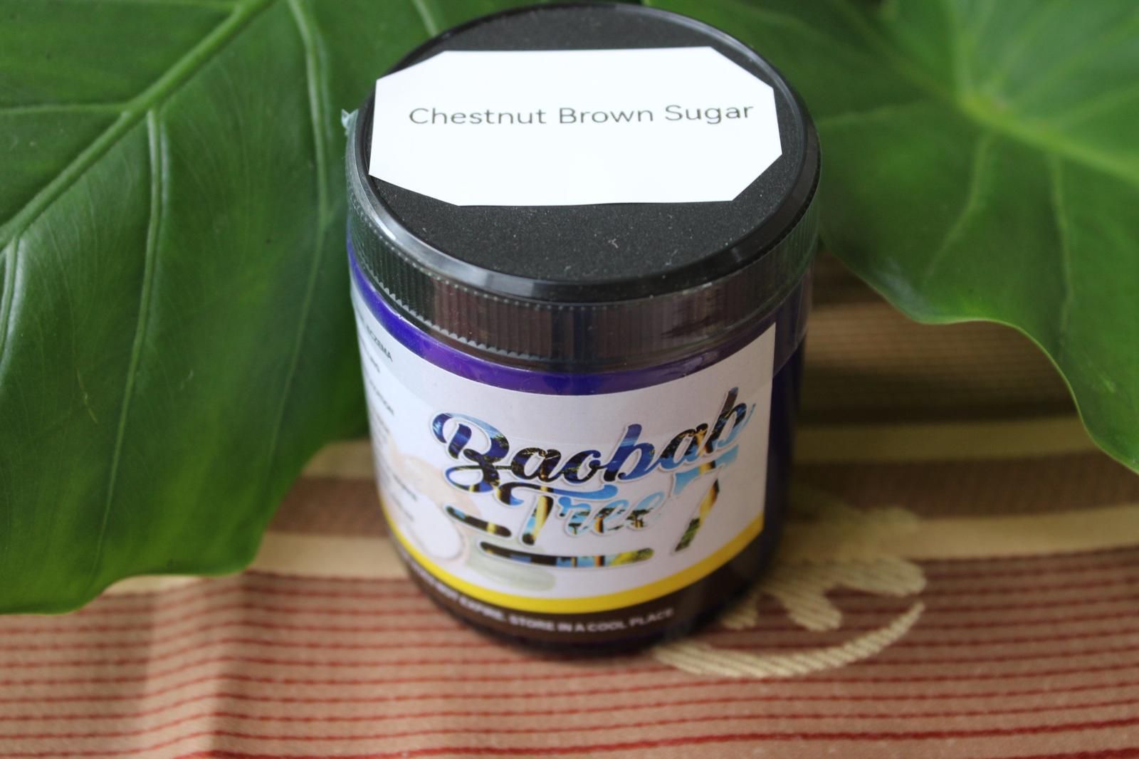 Jar of Chestnut Brown Sugar with a purple label, placed on a mat beside green leaves.