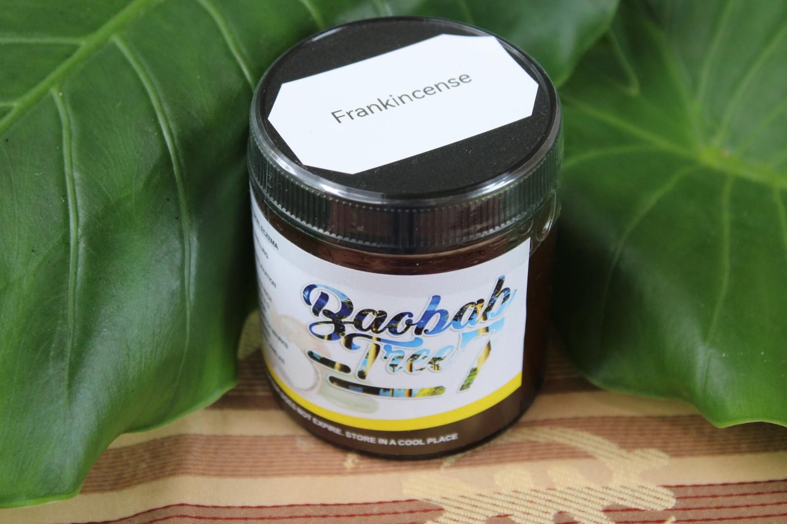 Baobab jam jar with white label and silver lid on a leaf-patterned wooden surface