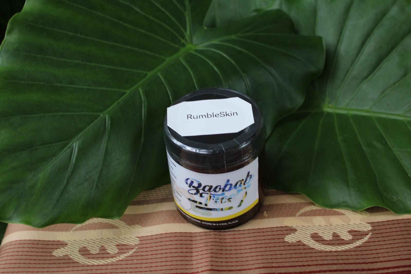 Small jar with a white label on a woven mat, in front of large green leaves.