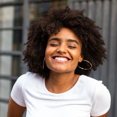 Smiling woman with curly hair in a white shirt against a blurred urban background
