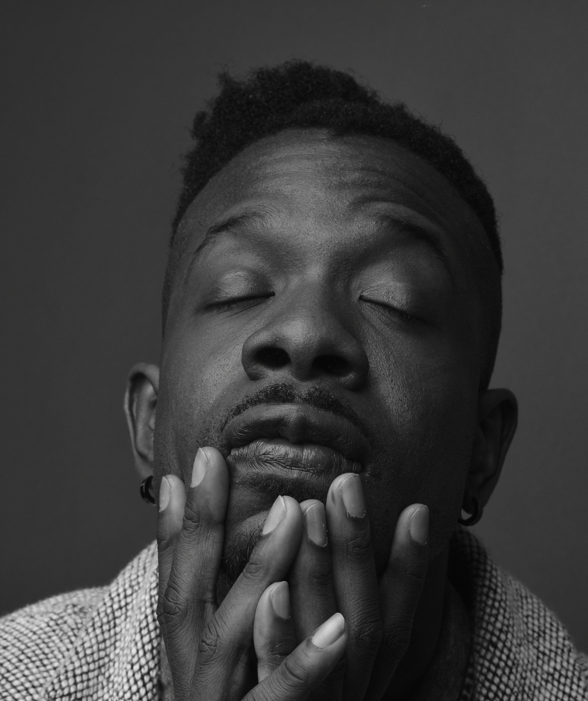 Close-up black-and-white portrait of a man with eyes closed, hands resting on his chin
