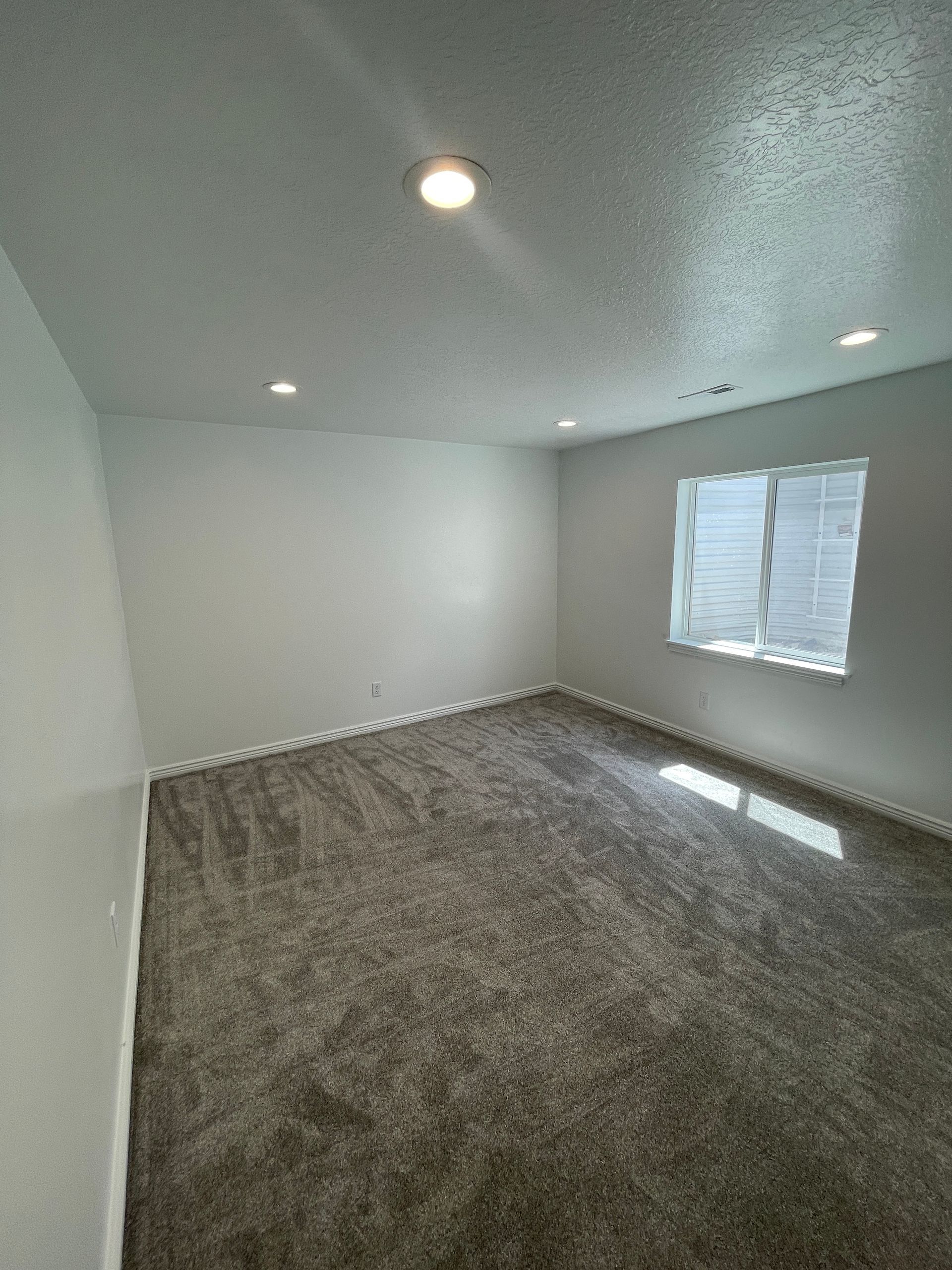 An empty room with a window and a carpeted floor.