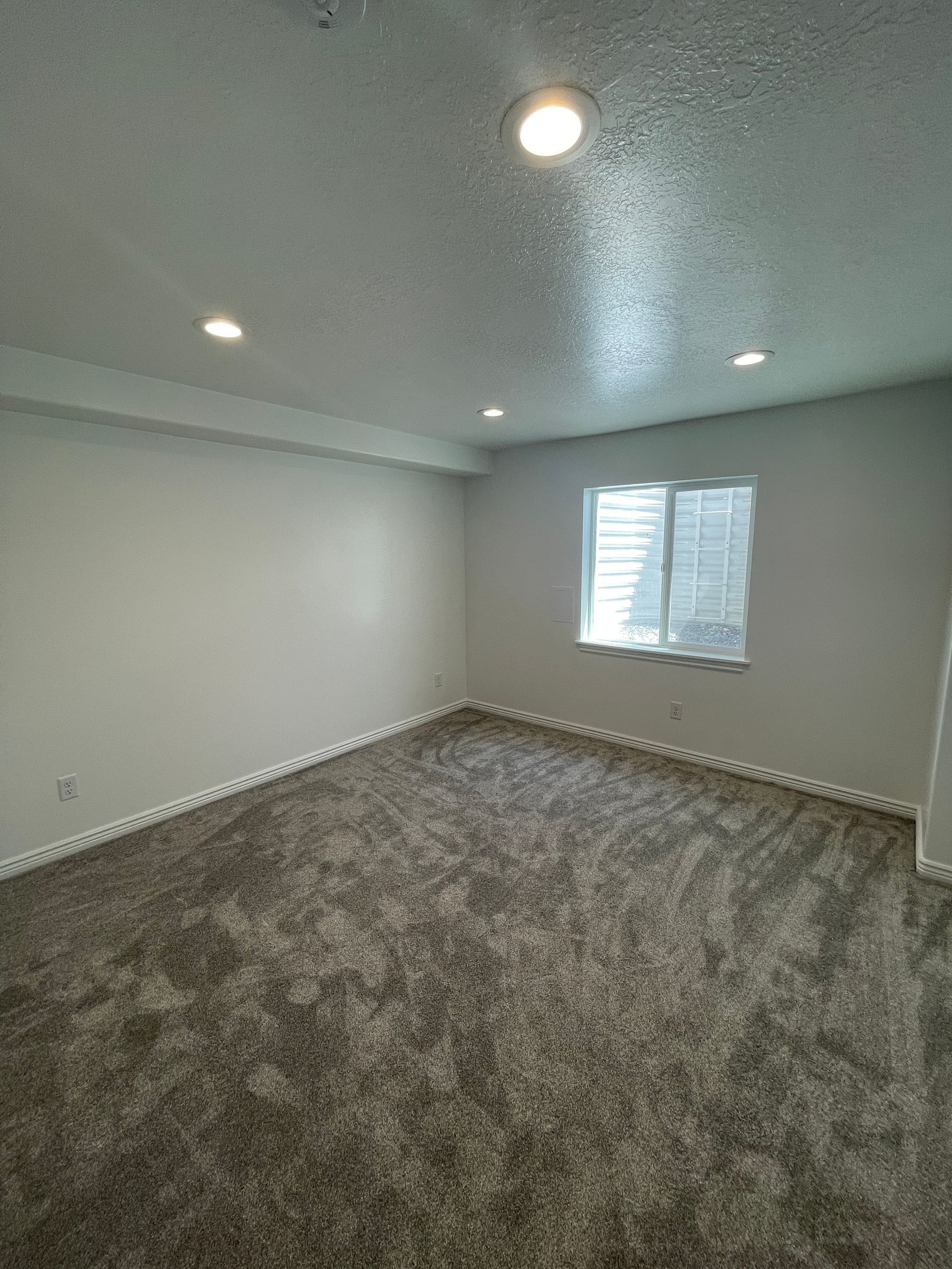A large empty room with a carpeted floor and a window.