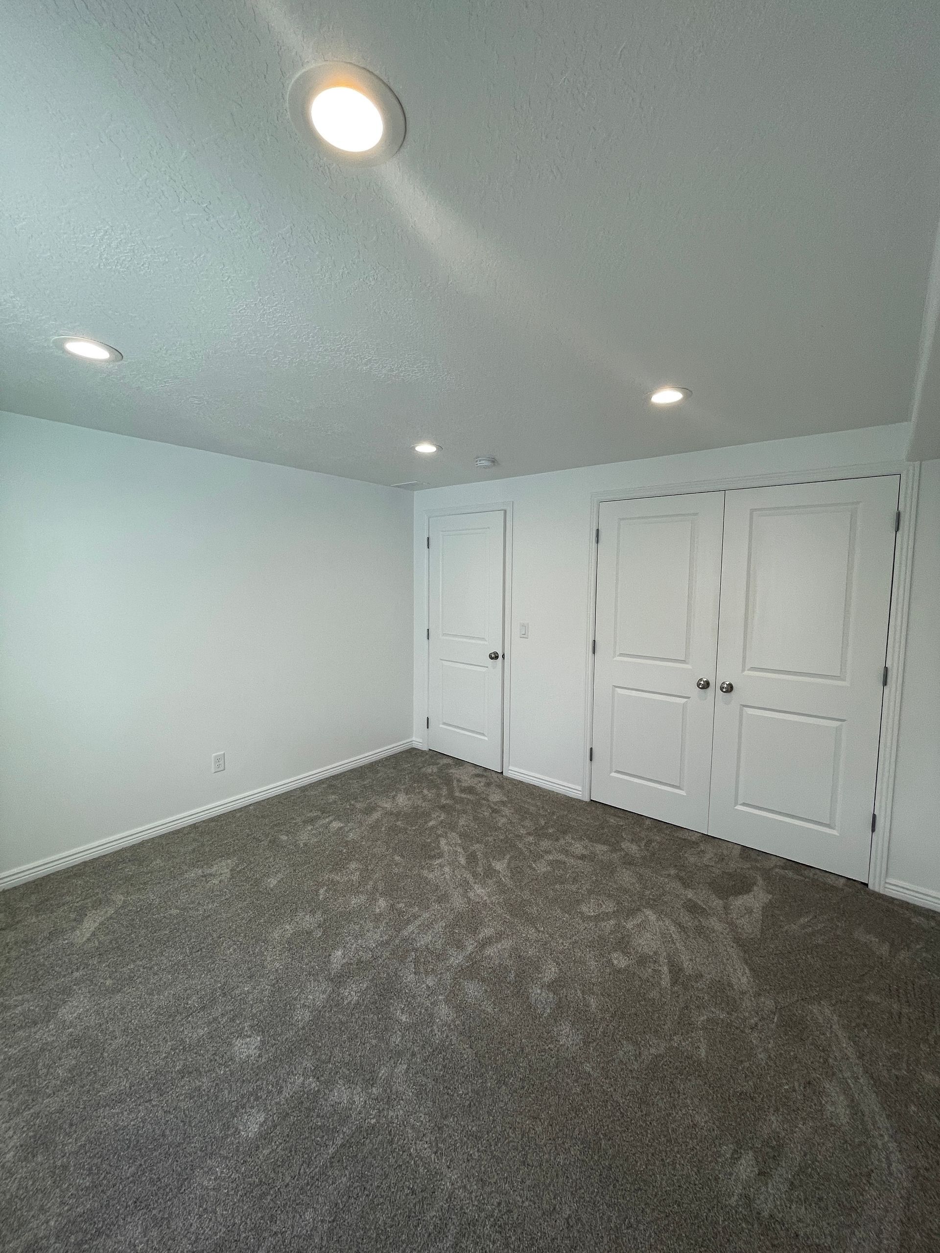 An empty basement with a carpeted floor and white walls.