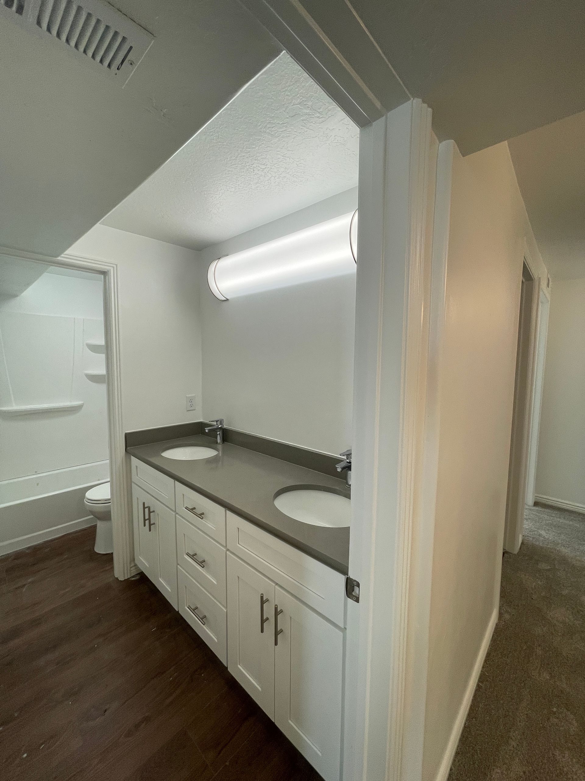 Small bathroom vanity with white cabinets, dark countertop, sink, mirror, and fluorescent light under a sloped ceiling