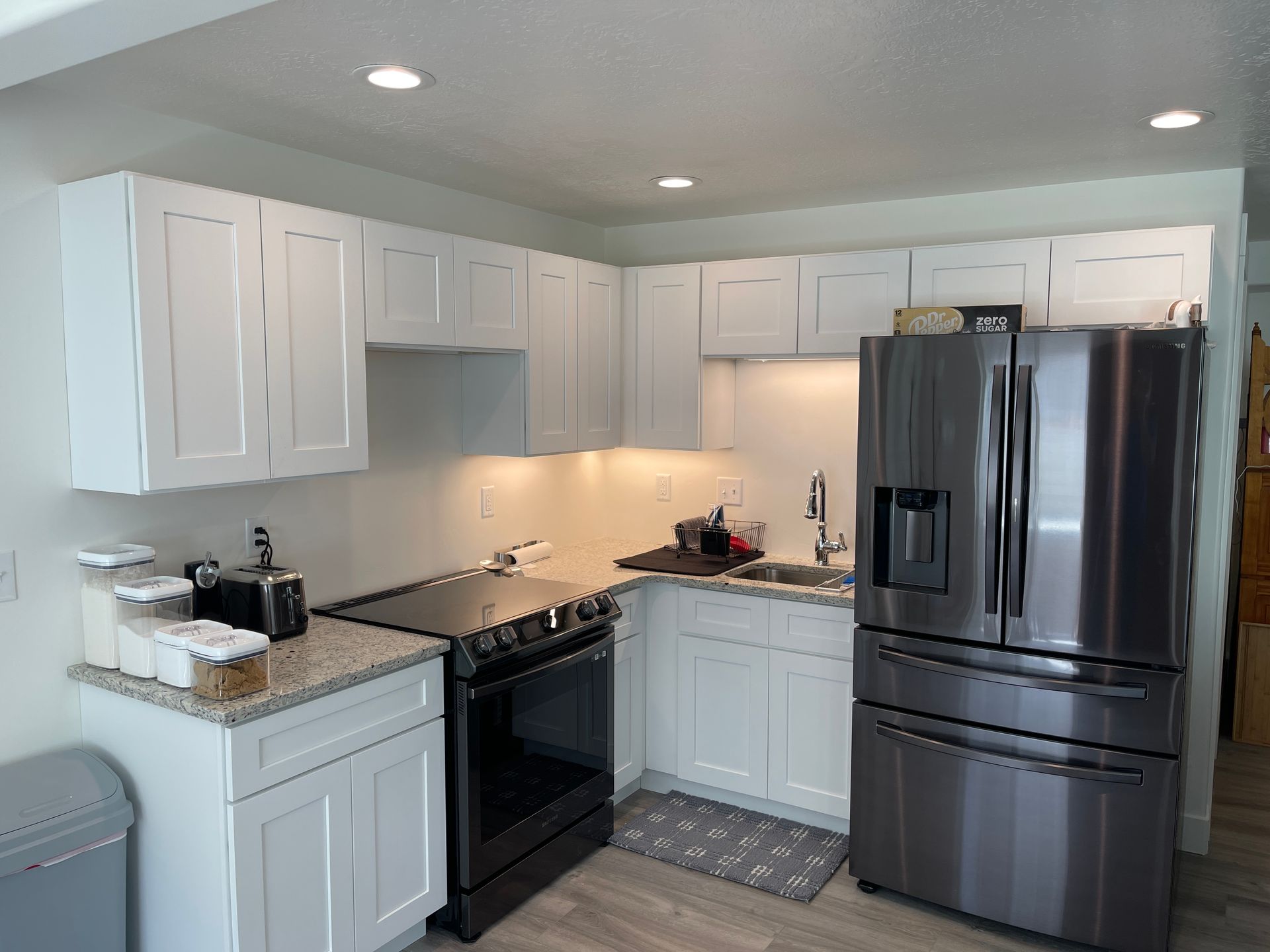 Bright white kitchen with stainless steel appliances, black stove, and light granite countertops
