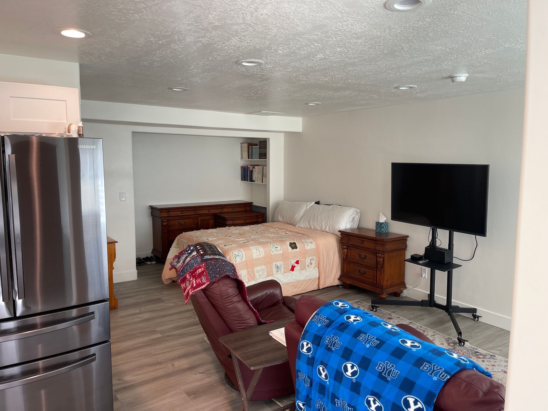 A living room with a bed , couch , television and refrigerator.