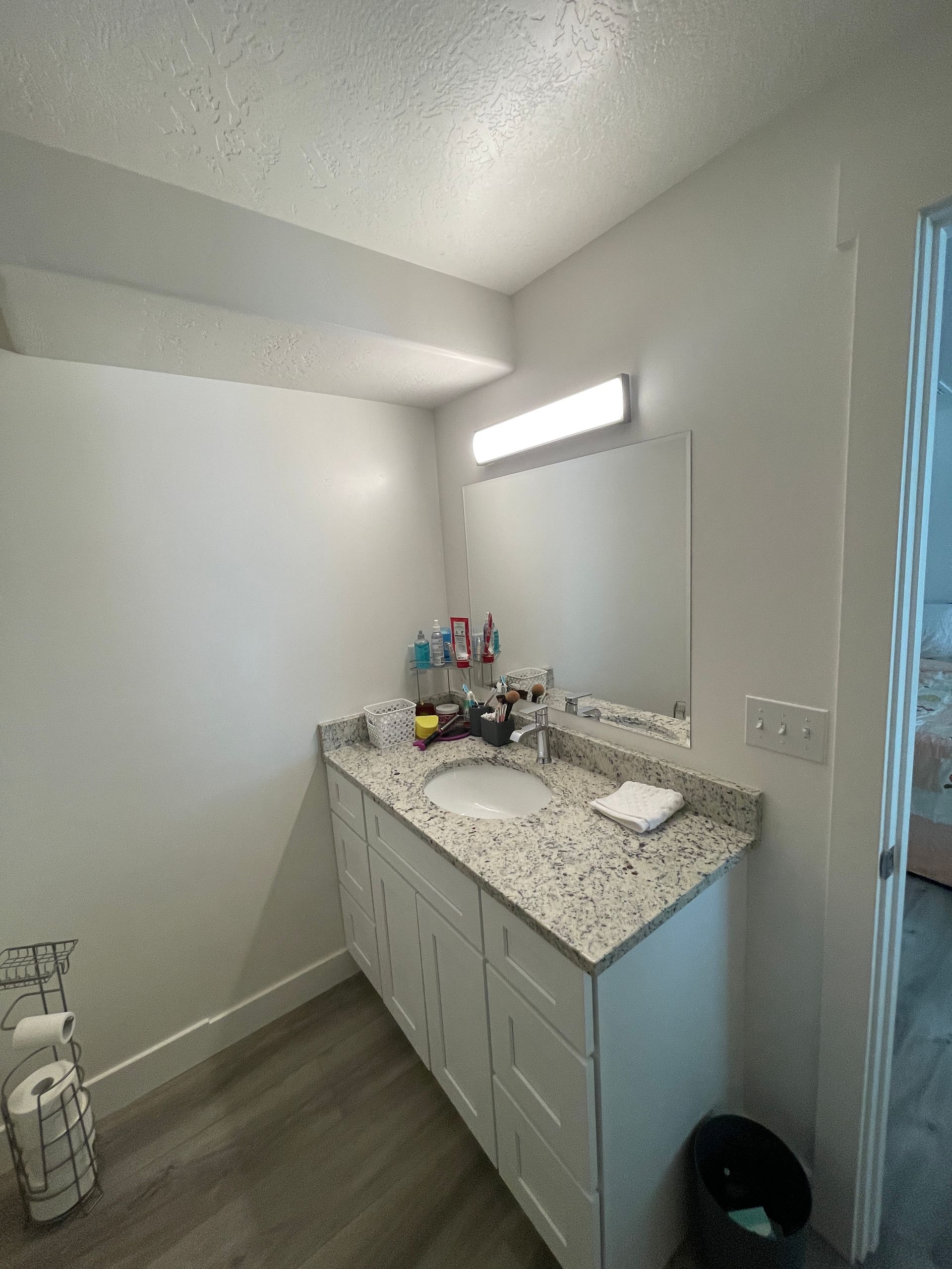 A bathroom with a sink , mirror and trash can.