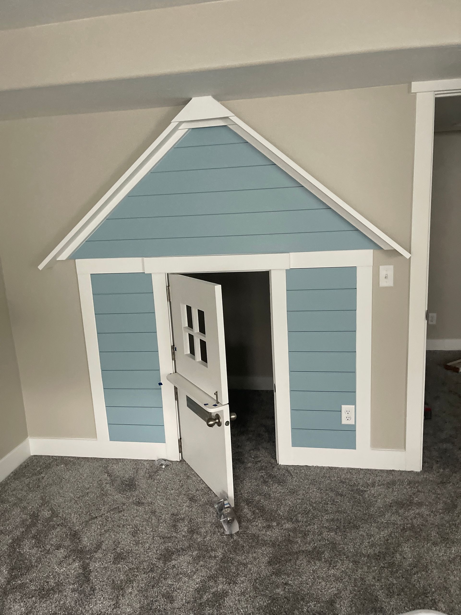 Small blue-and-white playhouse with an open door on gray carpet indoors