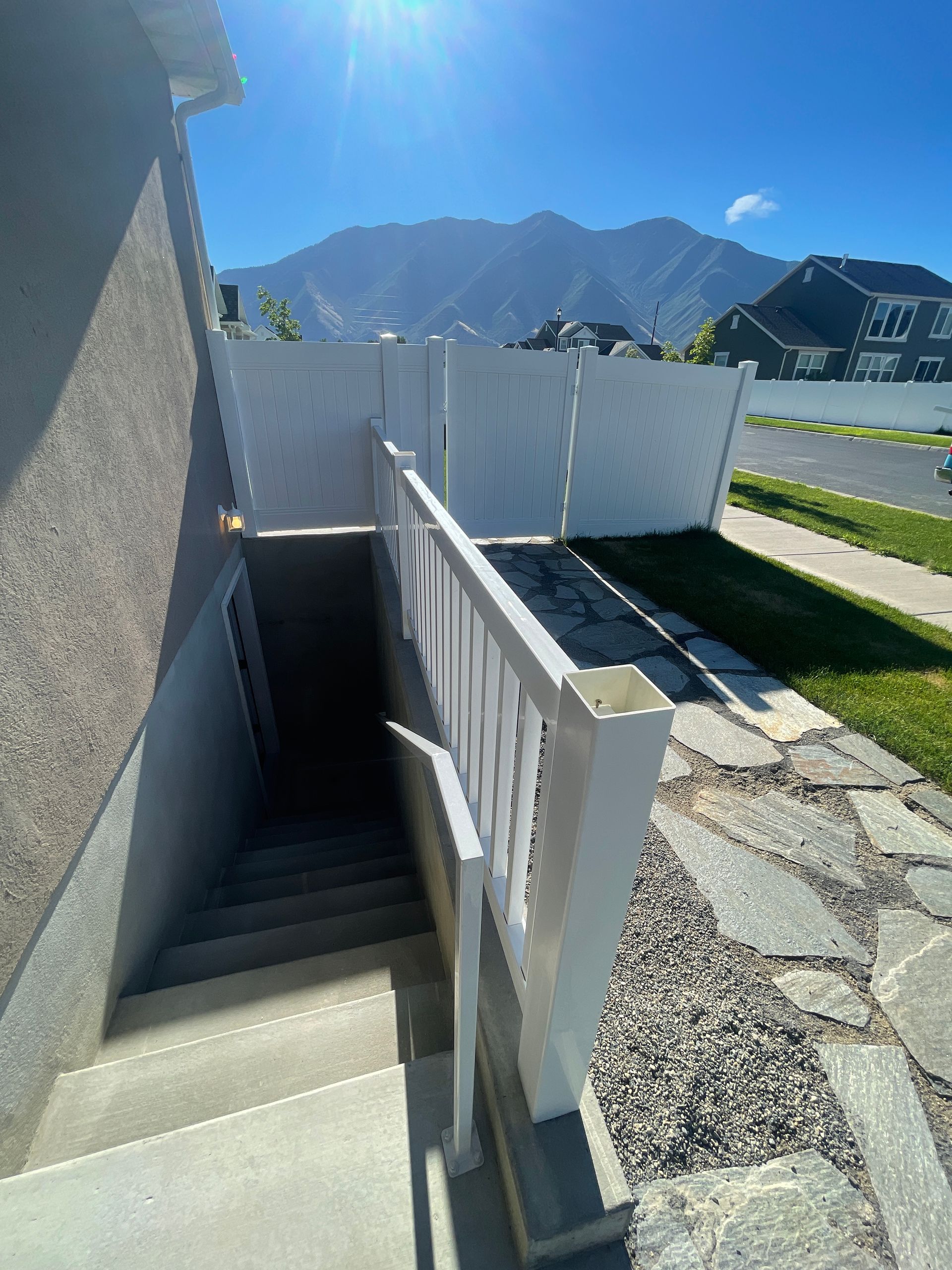A staircase leading up to a basement with a white fence and mountains in the background.