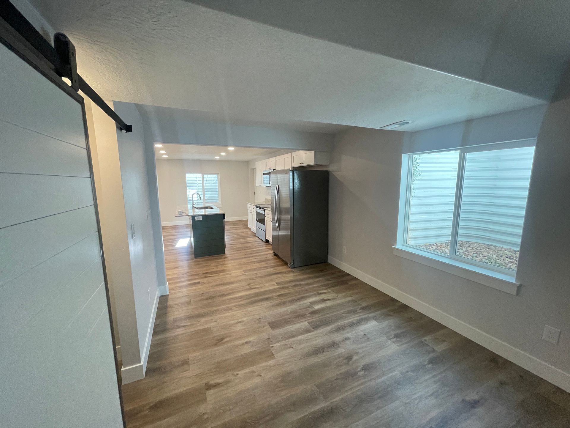 A living room with hardwood floors and a sliding barn door leading to a kitchen.