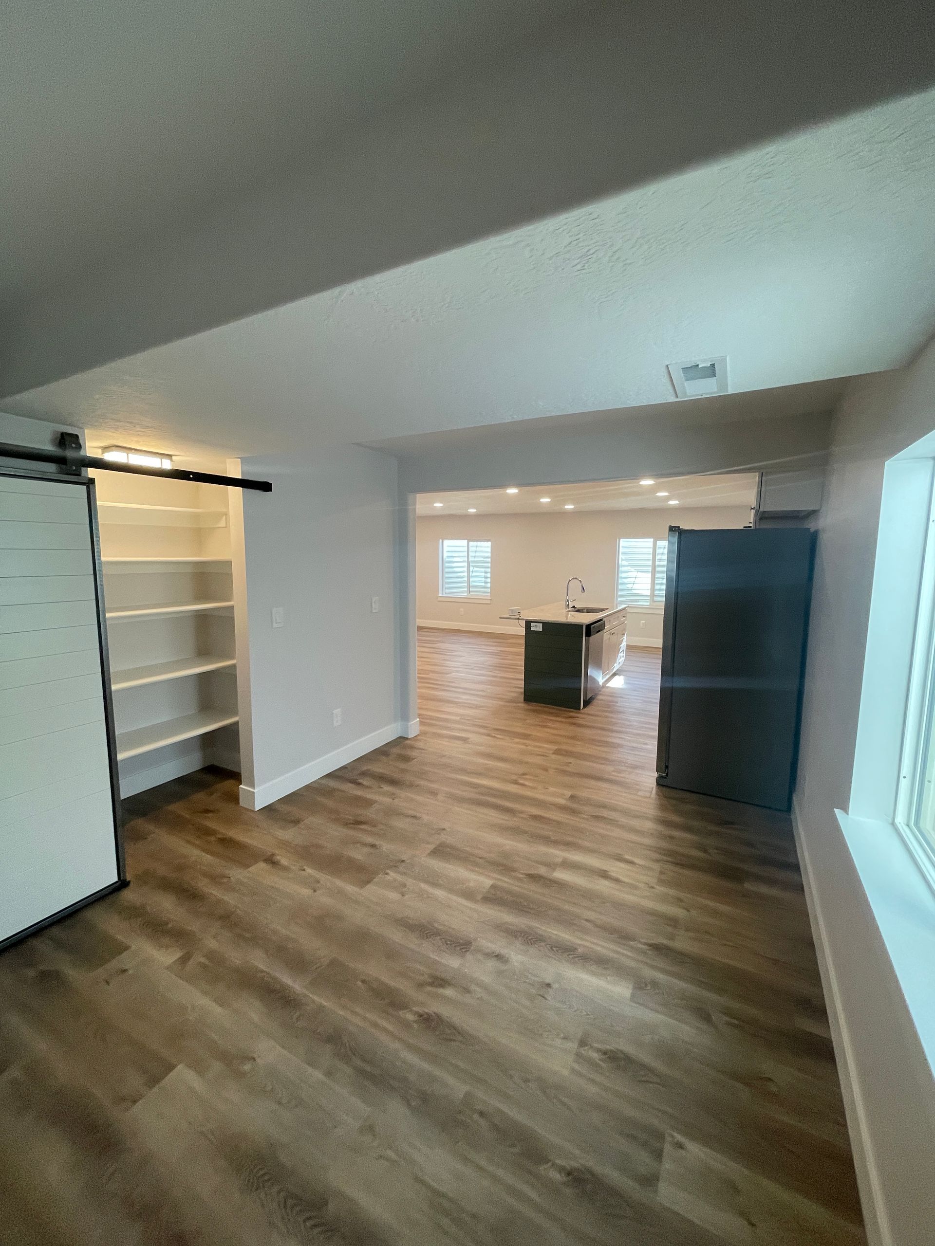 A living room with hardwood floors and a sliding barn door leading to a kitchen.