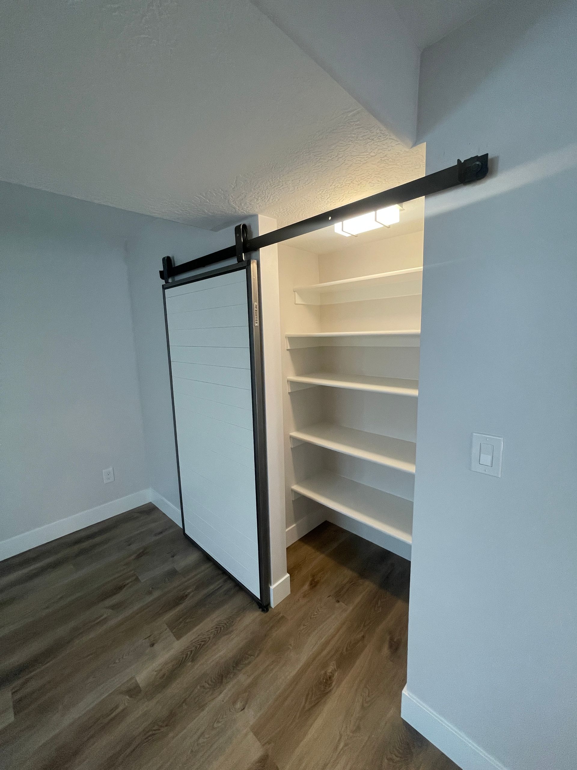 Open closet with sliding barn door, white shelves, and wood flooring in a small room