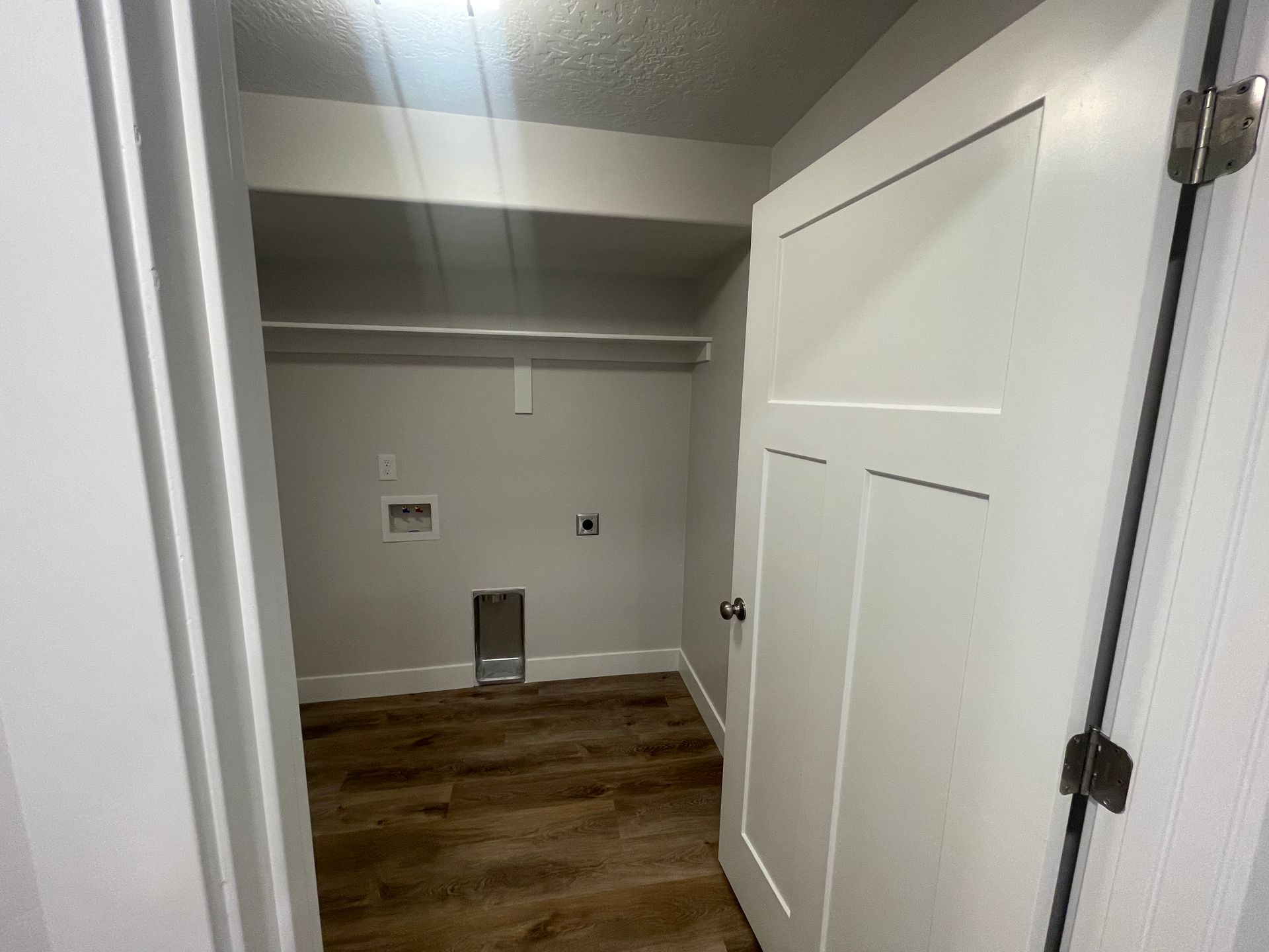 A laundry room with hardwood floors and a white door.
