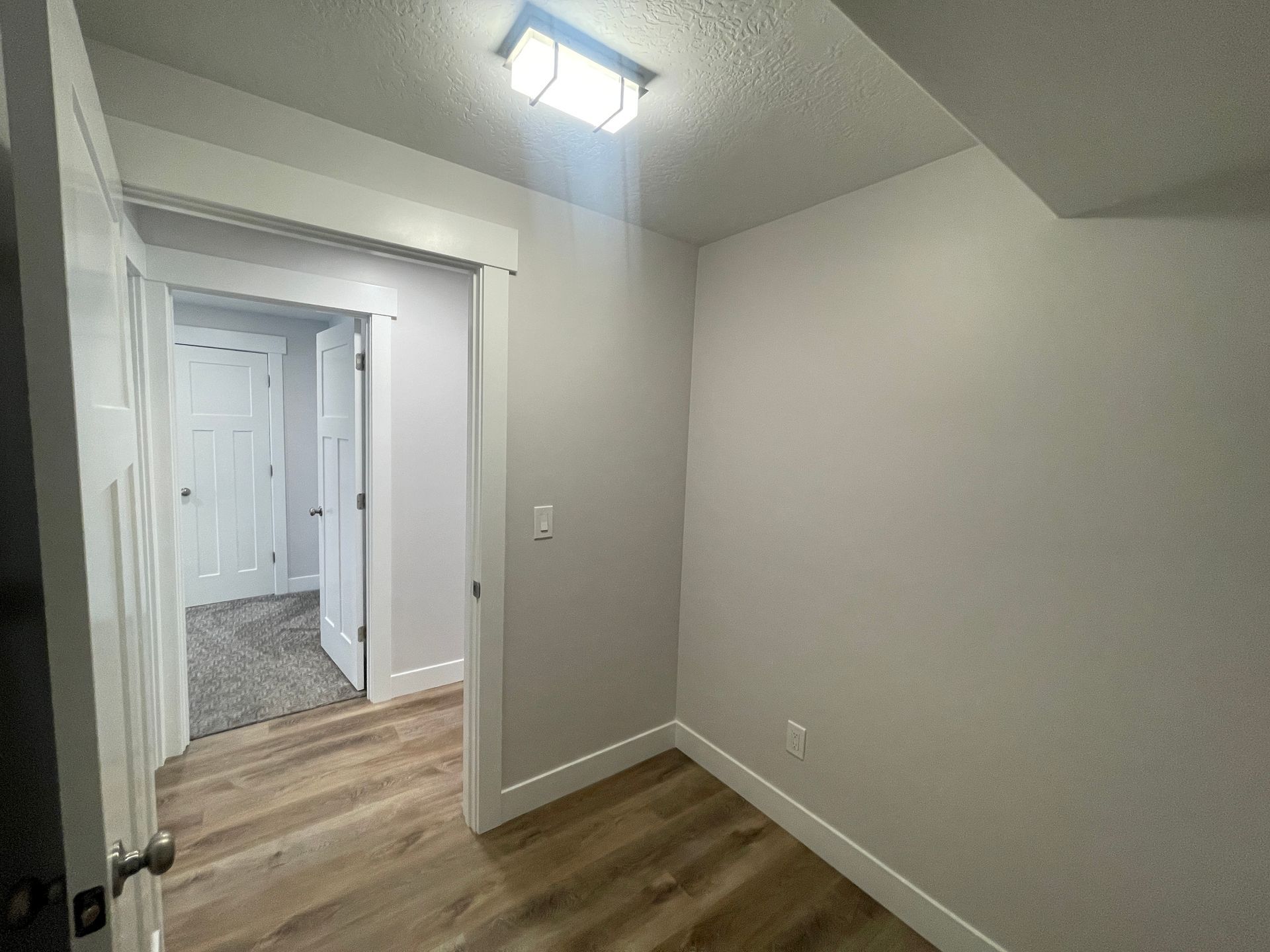 A small room with hardwood floors and a doorway leading to a hallway.