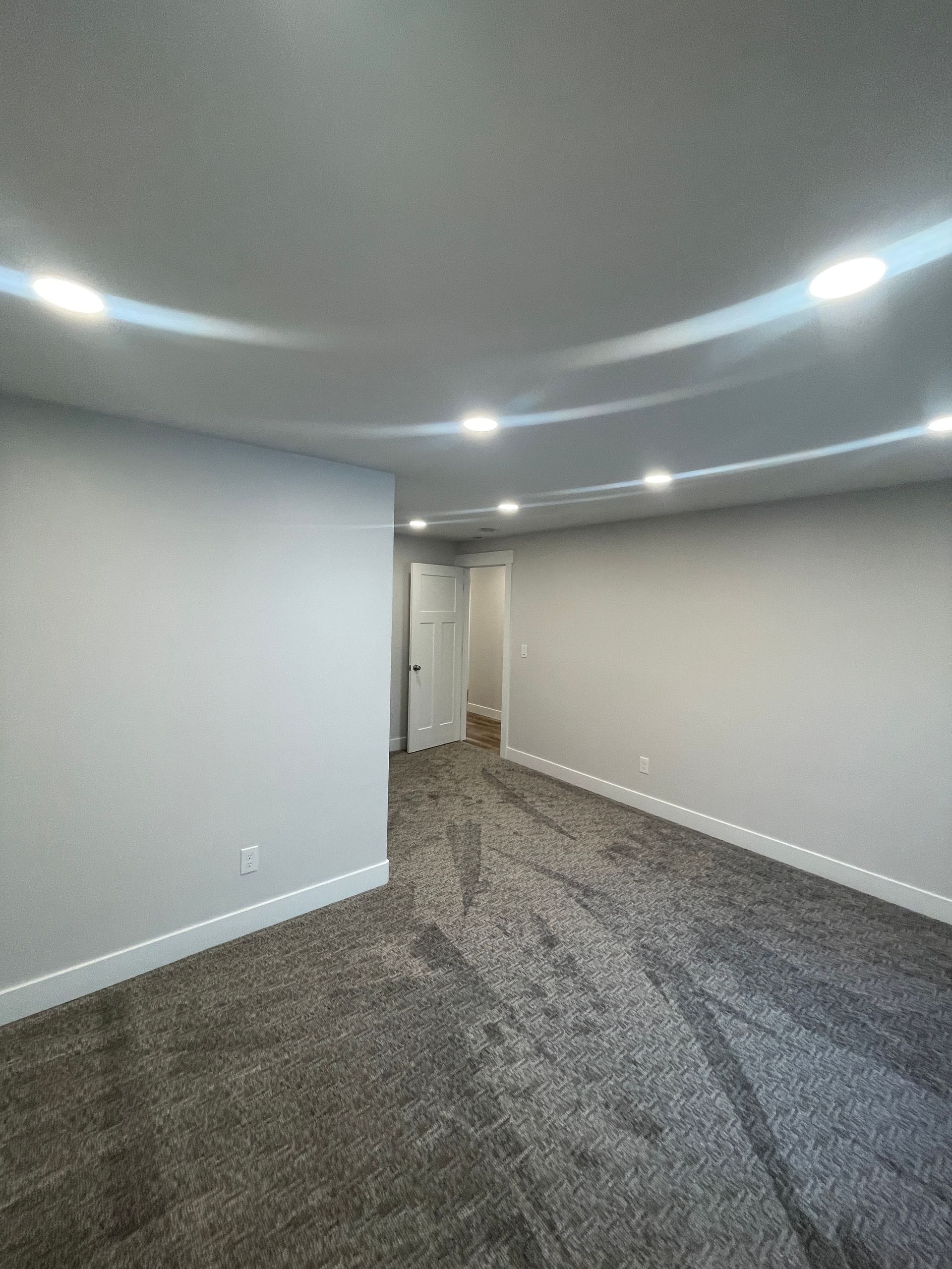 An empty basement with a carpeted floor and white walls.