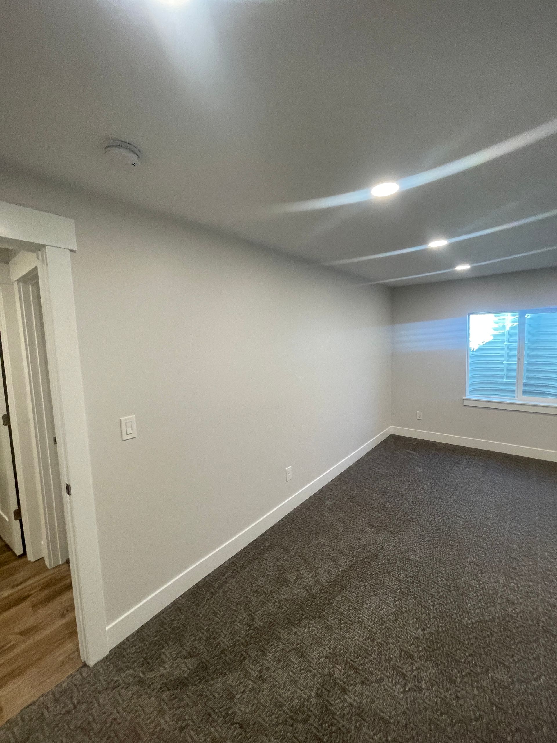 An empty living room with a large window and a carpeted floor.