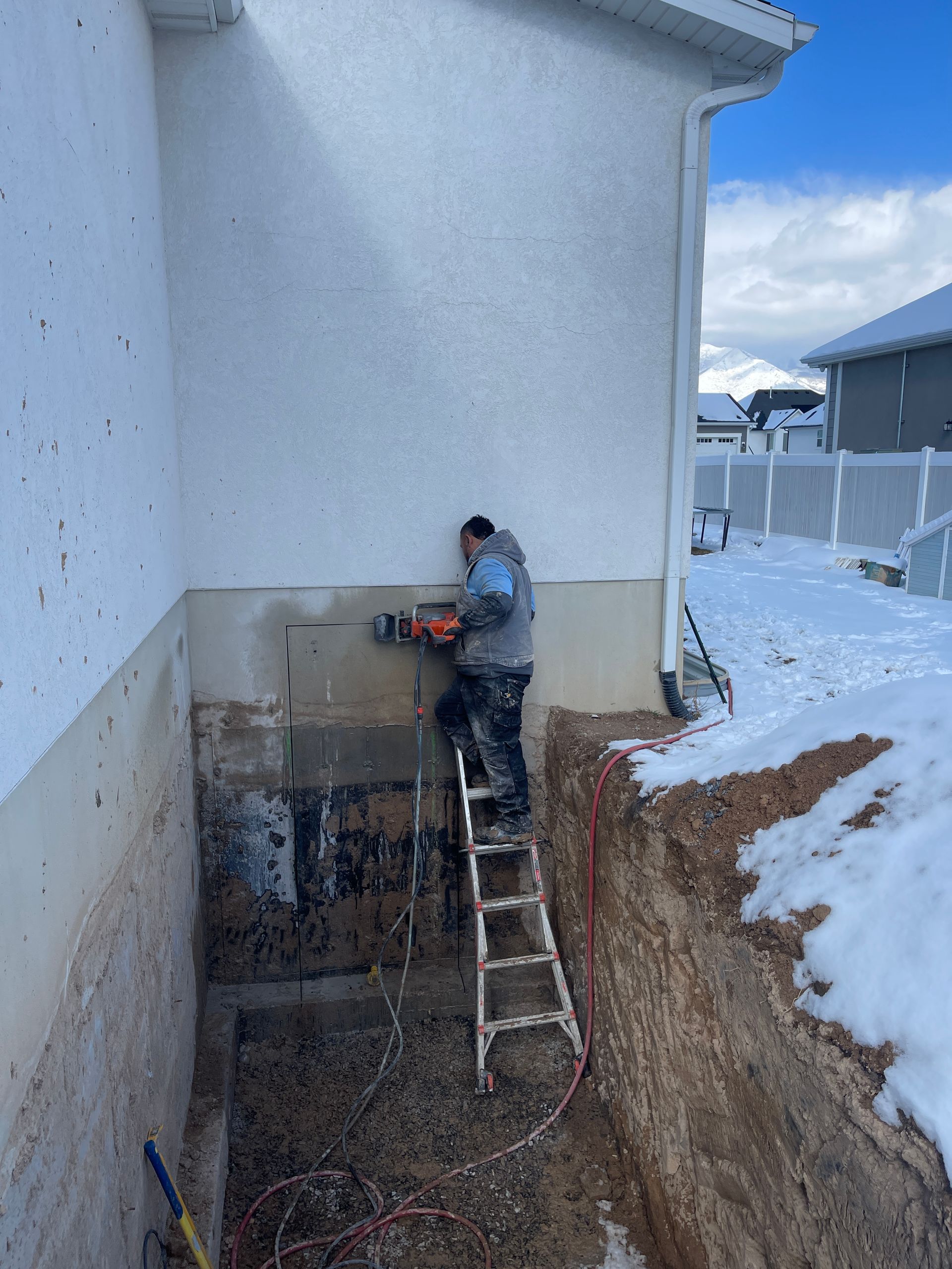 A man is standing on a ladder working on the side of a house.