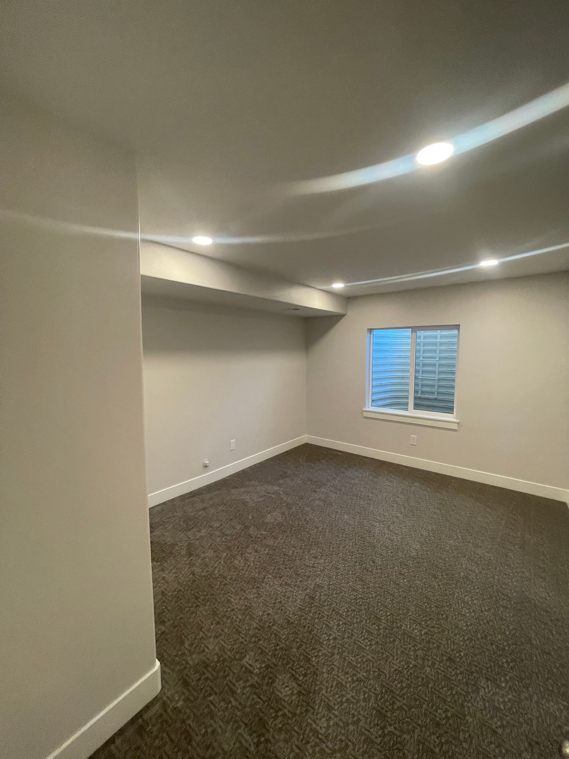 An empty room with a window and a carpeted floor.