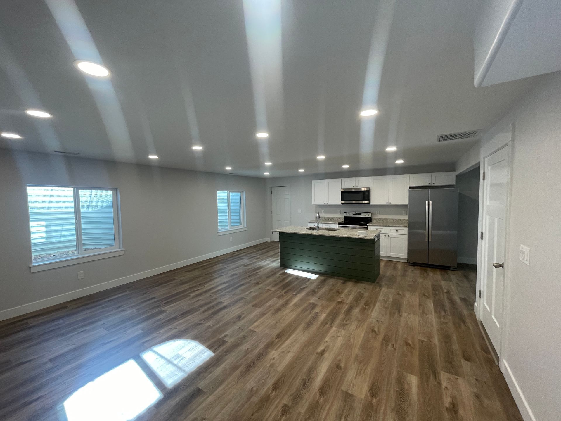 Empty modern kitchen and living area with gray walls, wood floors, island, and stainless steel appliances