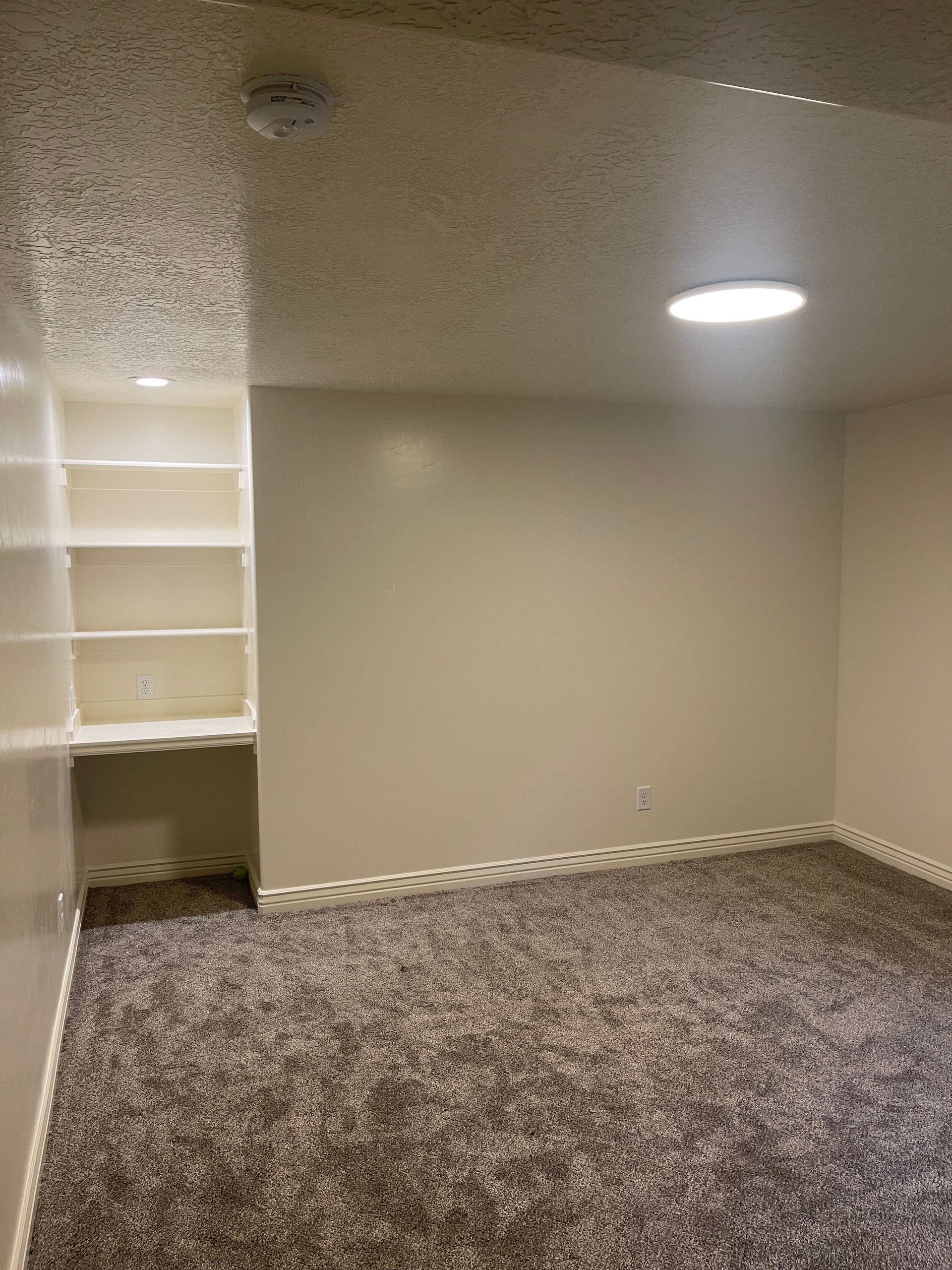 An empty room with a carpeted floor and a light on the ceiling.