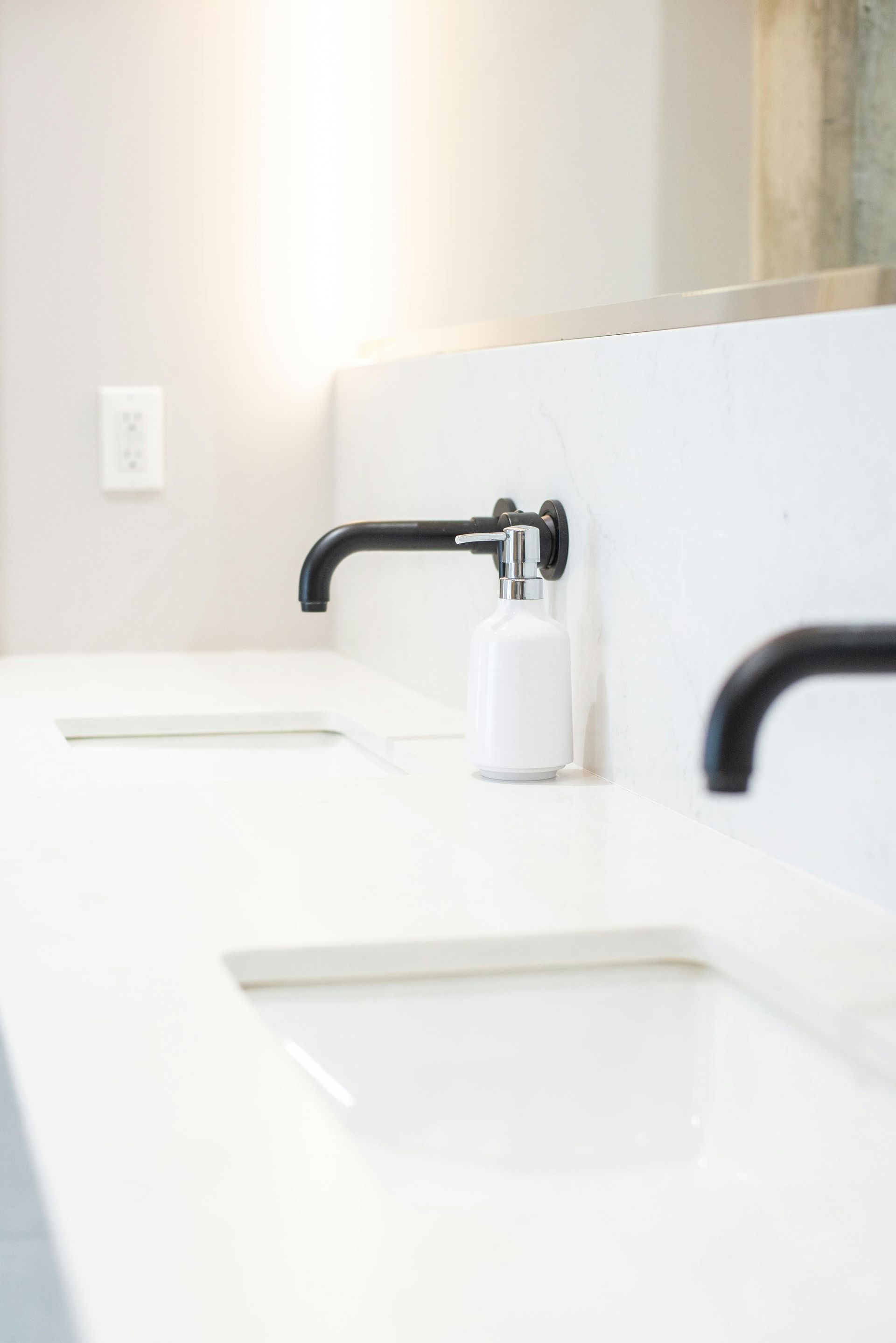 Bright bathroom vanity with black faucets, white sinks, and a soap dispenser.