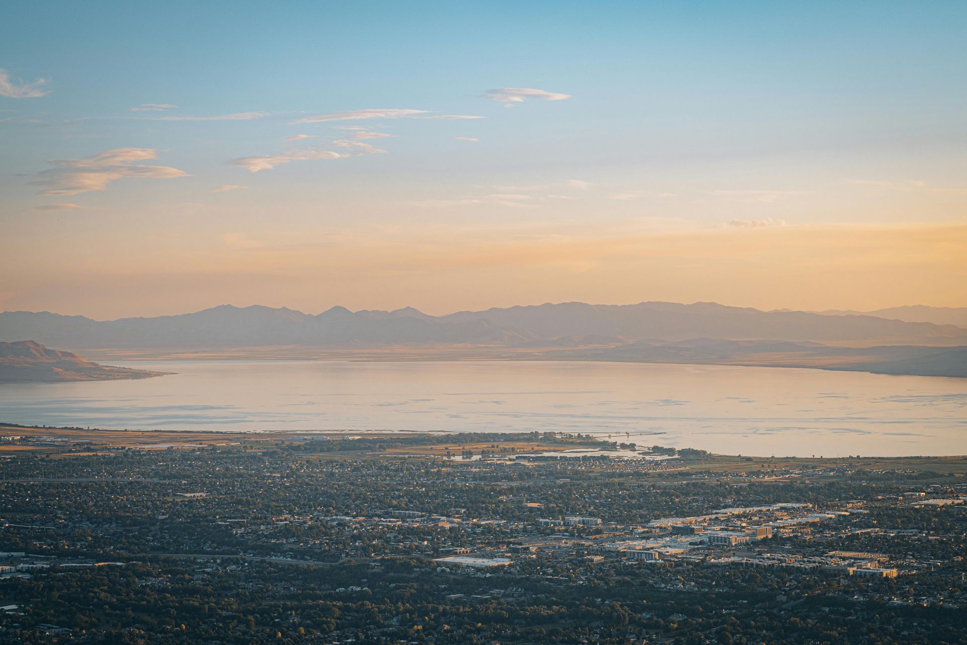 Aerial view of a Orem Utah and utah lake at sunset, with mountains on the horizon and warm pastel sky.
