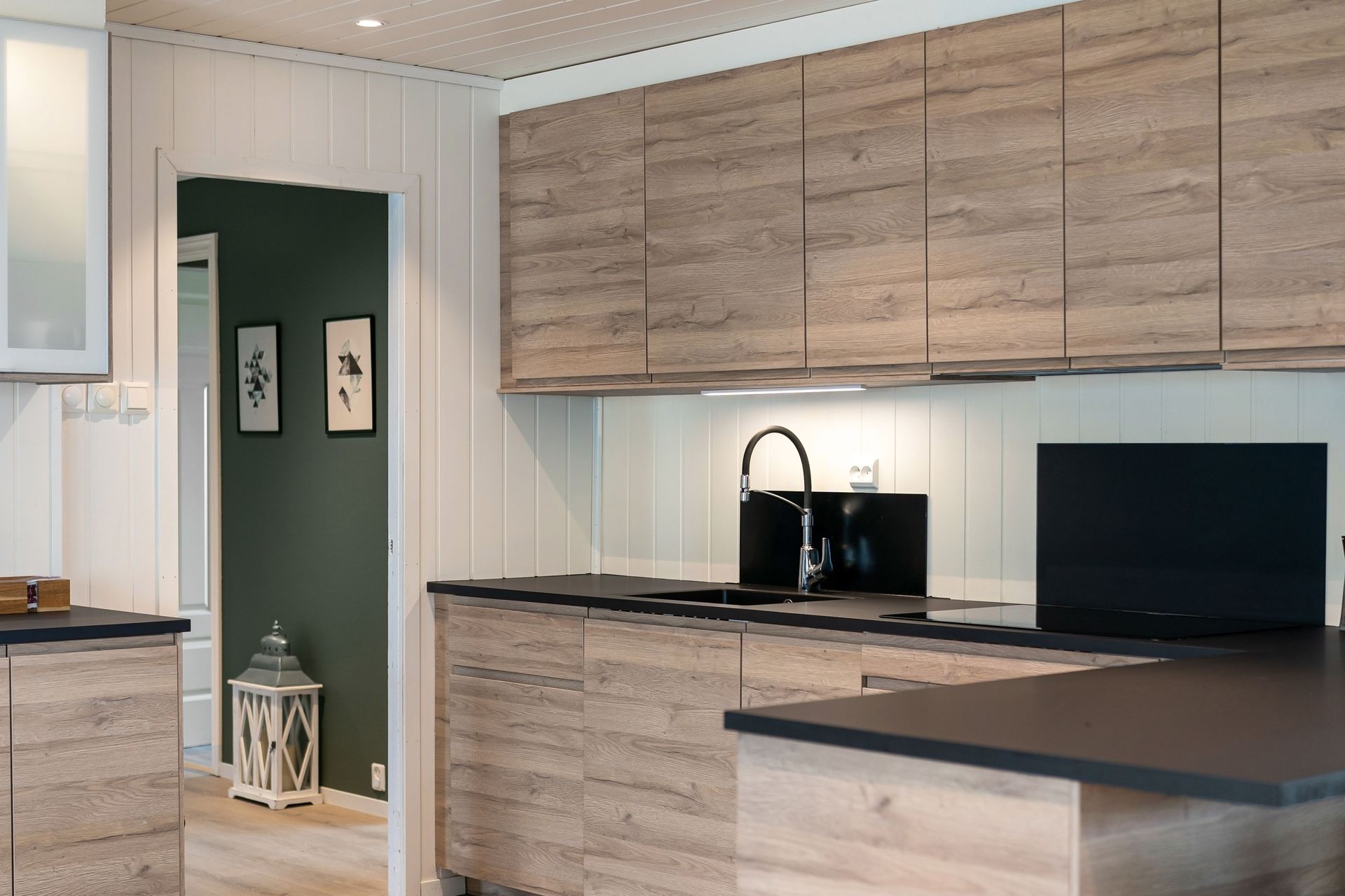Modern kitchen with wood cabinets, black countertops, and a dark green accent wall.