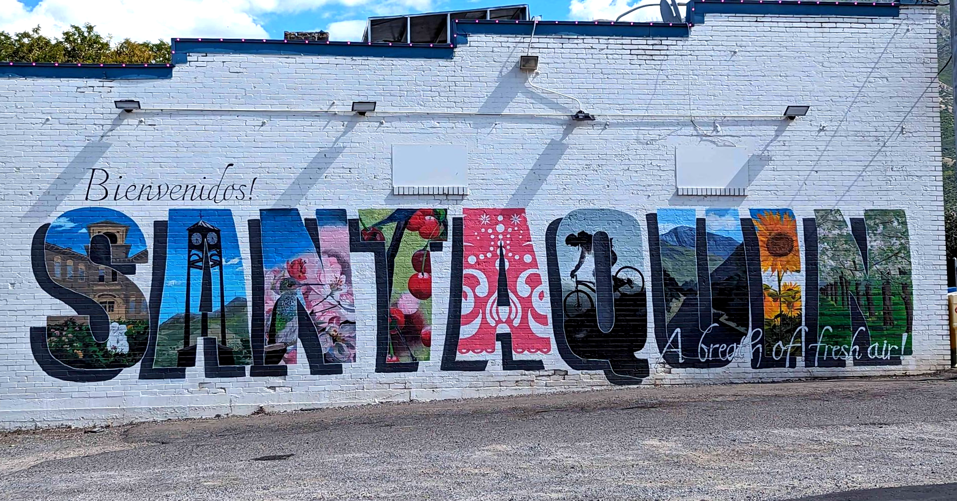 Colorful mural spelling “SANTANQUIN” on a white brick wall in an outdoor urban setting
