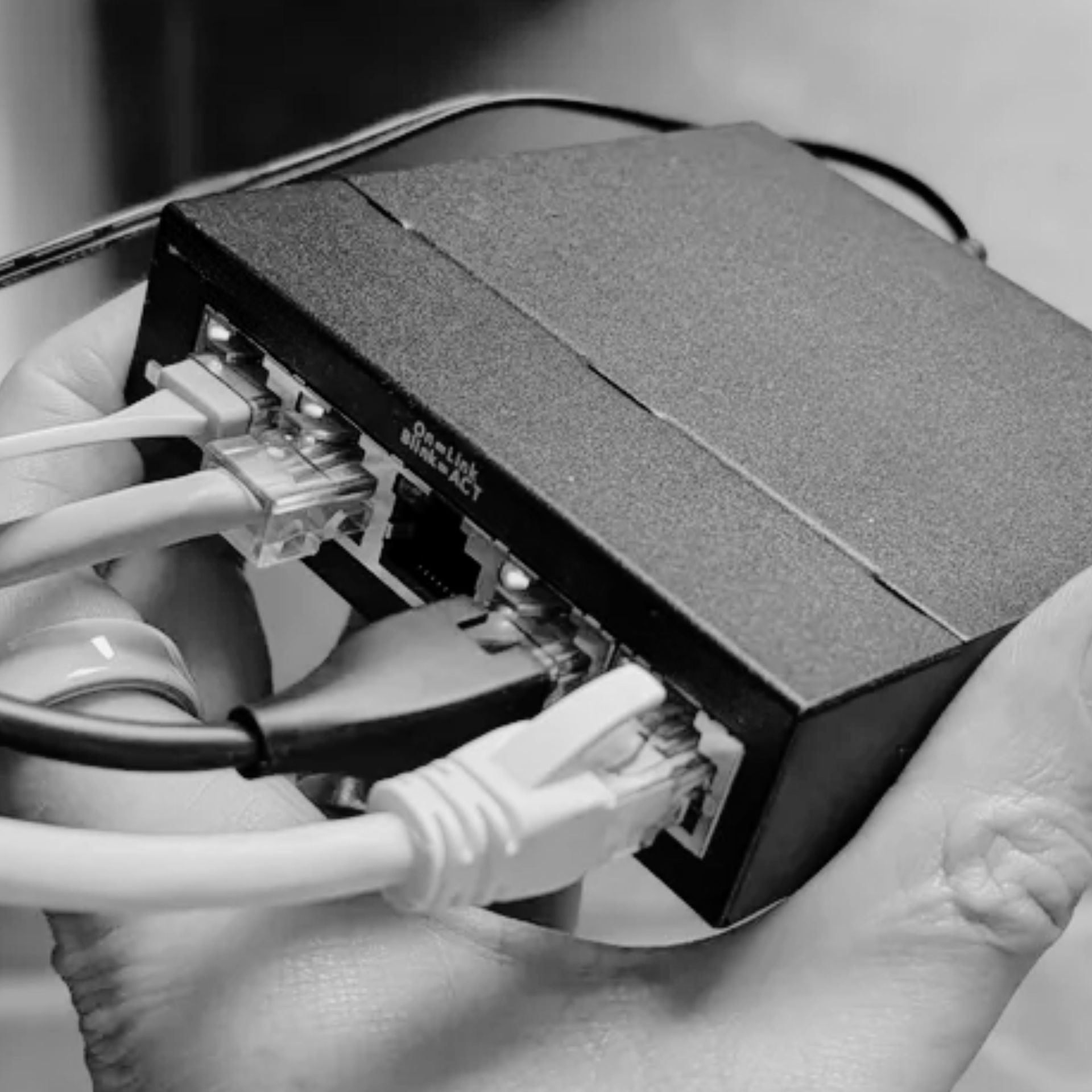 Hands holding a small black Ethernet switch with multiple white network cables plugged in