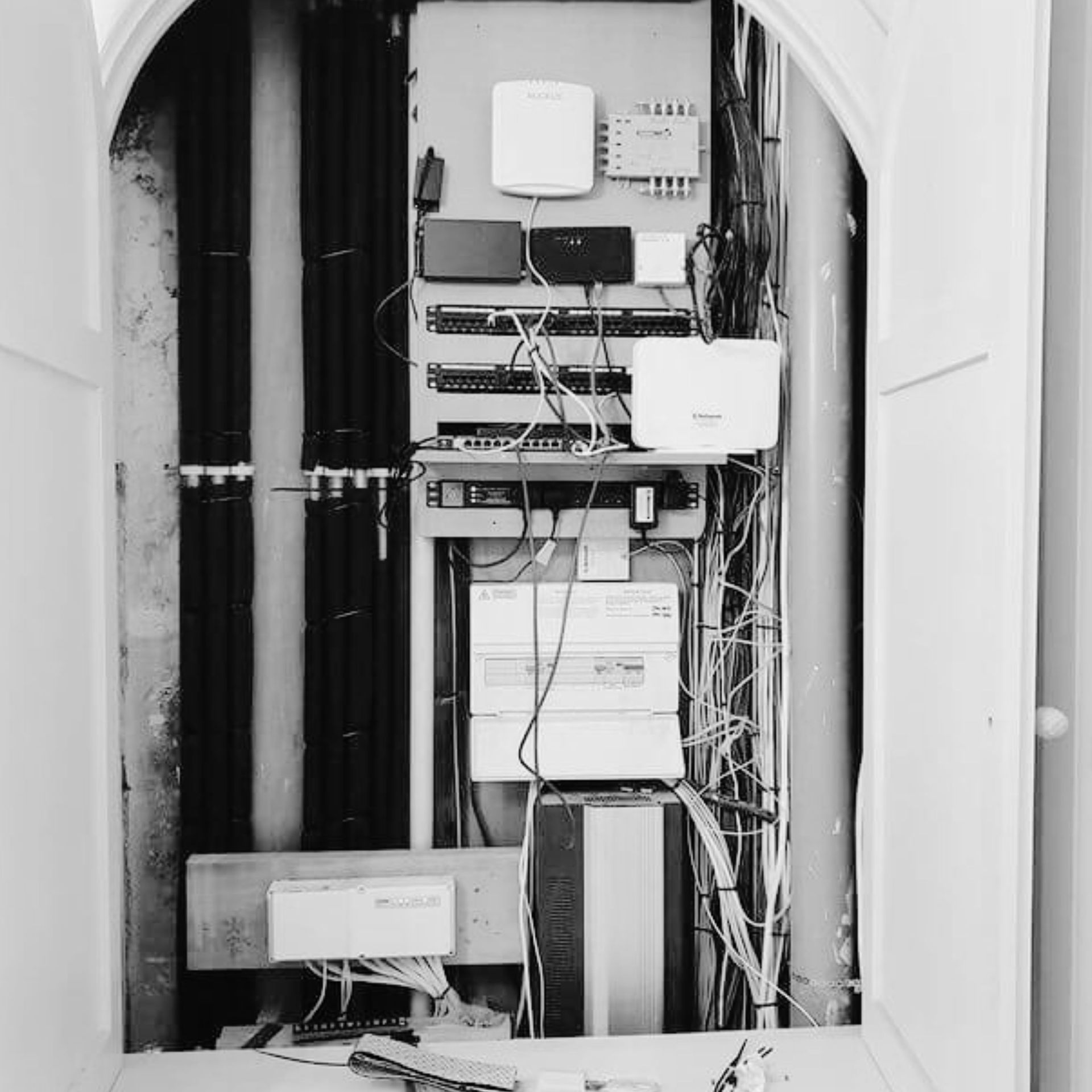 Open utility closet with electrical and network equipment, wires, and boxes mounted on the wall