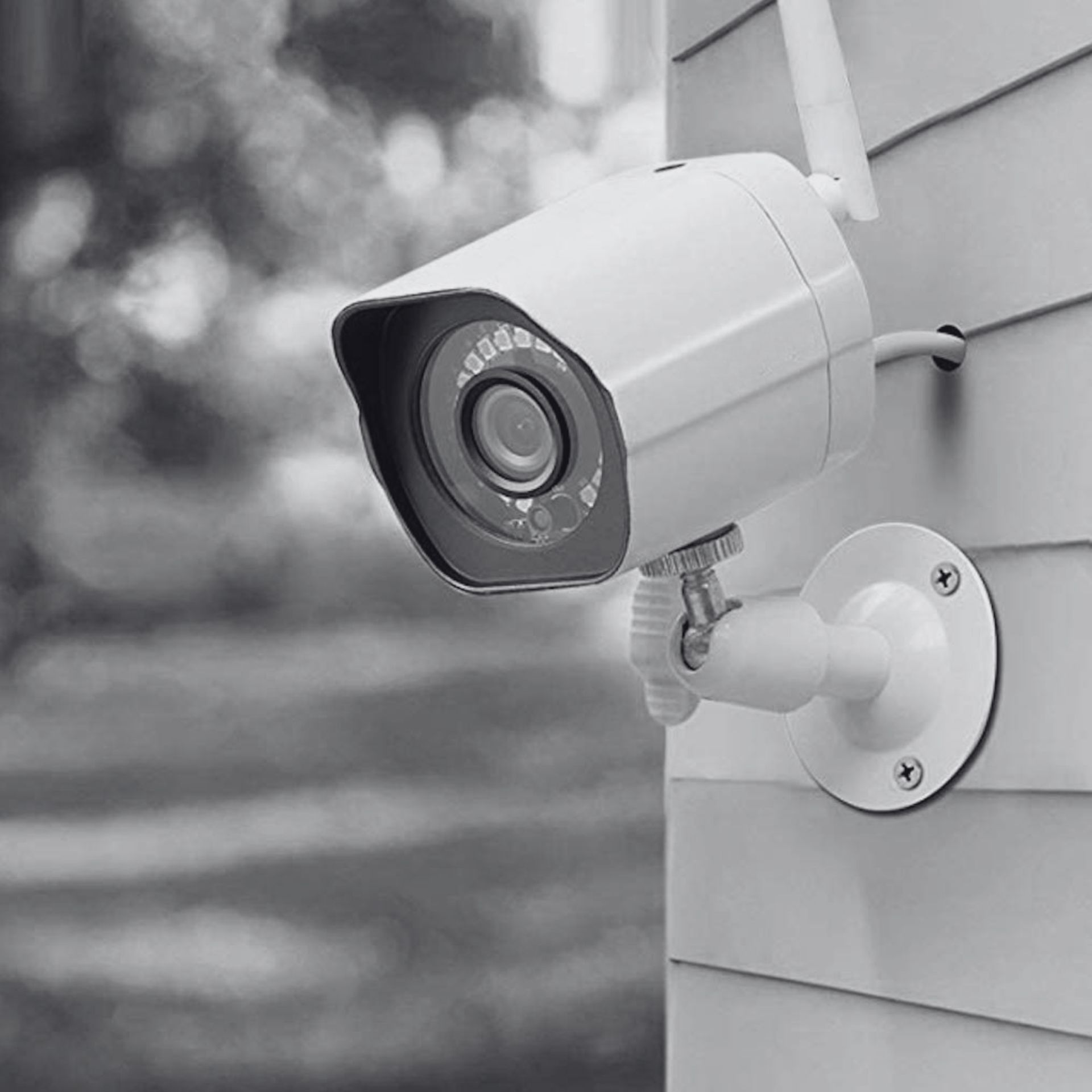 White security camera mounted on a house exterior, overlooking a yard.